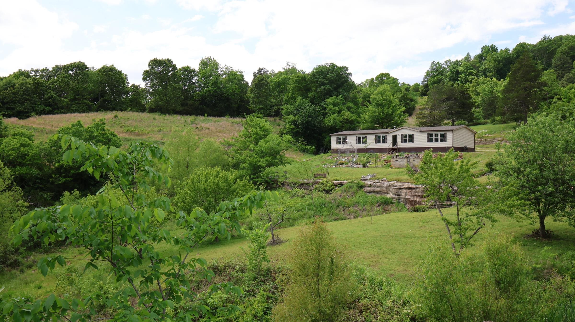 This 164.48-acre property offers live water, scenic views, privacy, a modern manufactured home, excellent hunting, and a rare mix of pasture and hardwood timber, all set in a private hollow with Ozark Mountain views.  The land features 7 natural springs, including one that creates a waterfall flowing into a year-round creek, along with 4 ponds, a drilled well, established trails, and an orchard with a variety of fruit trees. The 2021 manufactured home includes 5 bedrooms, 2 bathrooms, an open floor plan, updated appliances, spacious kitchen, walk-in closets, a large walk-in shower, and a soaking tub. A whole-house backup generator provides added security. Additional improvements include 3 shops (two 30x50 and one 30x40) with concrete floors, ideal for equipment, storage, or workspace. Wildlife is abundant, with deer, turkey, and black bear frequently seen. Highway 9 frontage offers easy access while maintaining privacy. Conveniently located minutes from the White River, under an hour to Norfork Lake, and about 20 minutes to Mountain View (home of the renowned Ozark Folk Center, live music, and year-round festivals), this is a one-of-a-kind Ozark property all for $734,900!