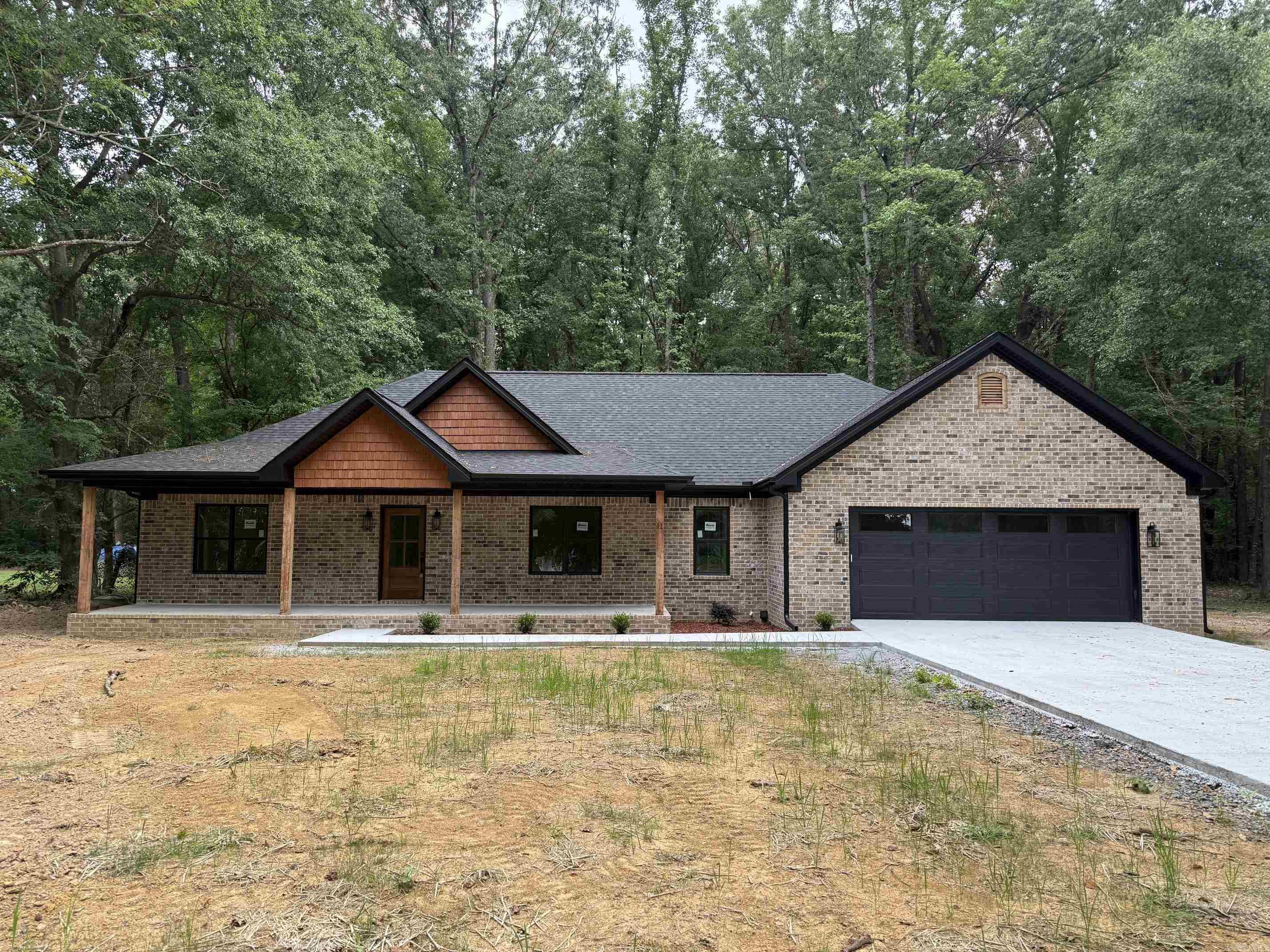 New construction home nestled on a private, wooded lot offering peace, space, and modern style. This thoughtfully designed home features an open-concept layout with a spacious living area, soaring ceilings, and a striking exposed beam. The kitchen is a standout with custom cabinetry, a large island, quartz countertops, and stylish lighting—perfect for entertaining.  The primary suite includes a spa-like bath with a tiled walk-in shower and double vanity. Additional highlights include a dedicated laundry room with built-in cabinetry, generous storage throughout, and a covered front porch ideal for relaxing and enjoying the natural surroundings.  Exterior features a classic brick finish with warm wood accents and a sleek dark garage door for great curb appeal. Located in a quiet setting with no restrictions, giving you the freedom to truly make it your own.