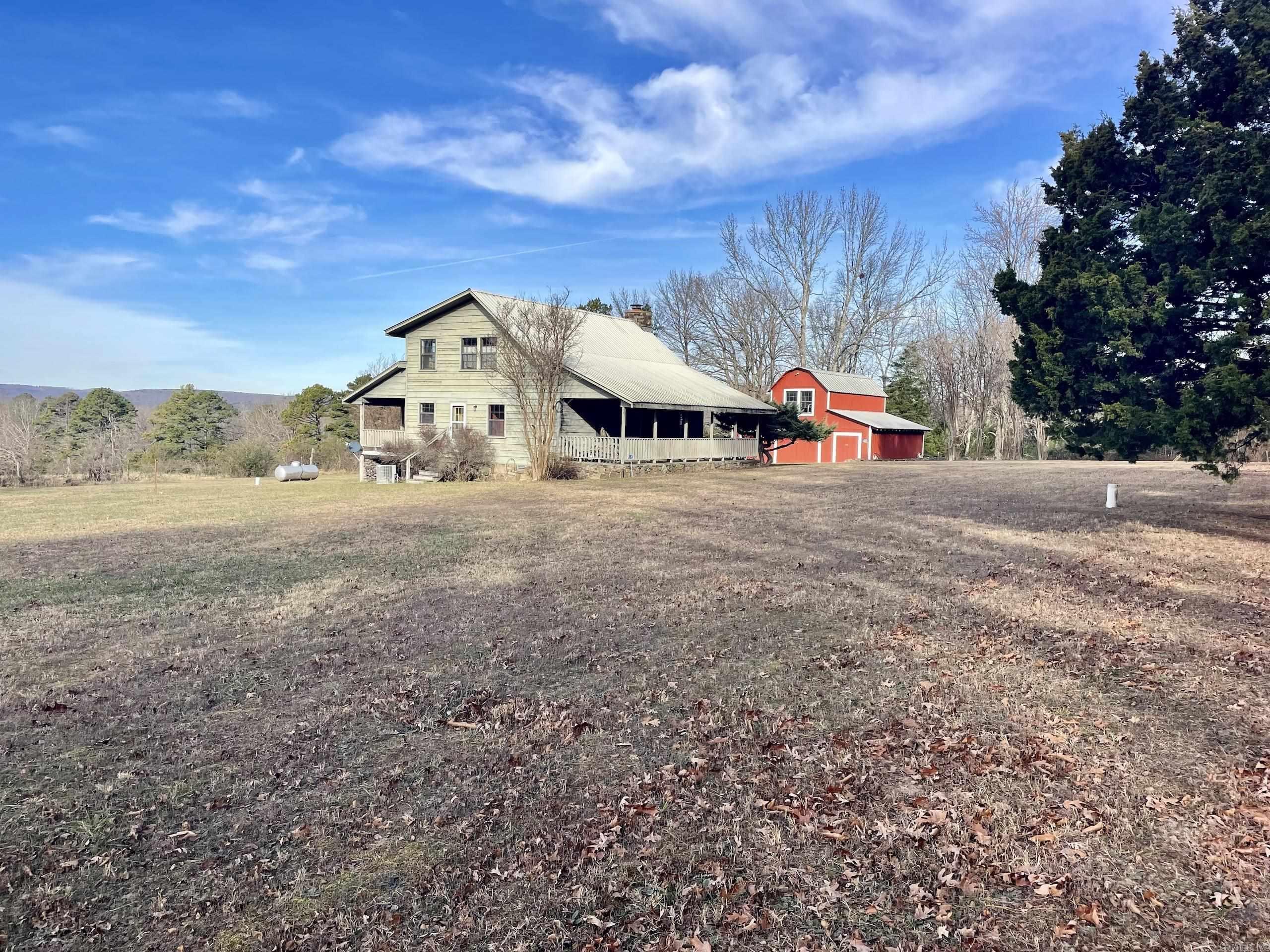 This scenic Ozark Mountain farm features paved frontage on two county roads and a gated private drive, offering privacy with easy access. Located in the Arkansas Ozarks, the property includes county water, electricity, and high-speed internet for comfortable rural living. Three residential structures include a historic farmhouse ready for restoration, a well-maintained secondary home, and a versatile barndominium.  The primary residence is a 1,250± sq ft, two-story home with three bedrooms, two bathrooms, central heat and air, a wood-burning fireplace, and expansive front and back porches with panoramic Ozark Mountain views. The barndominium offers central HVAC, a full bath, upstairs bedroom, and large barn doors—ideal for guests, rental income, or entertaining.  The farm is fully fenced and cross-fenced for livestock, with four barns, a steel pipe working pen with water and electricity, and five ponds. Approximately 115± acres of improved Bermuda and fescue pasture support grazing and hay production. Timber and abundant wildlife, including deer and turkey, add hunting and investment appeal. Ideal for a cattle operation, horse farm, hunting property, or family estate.