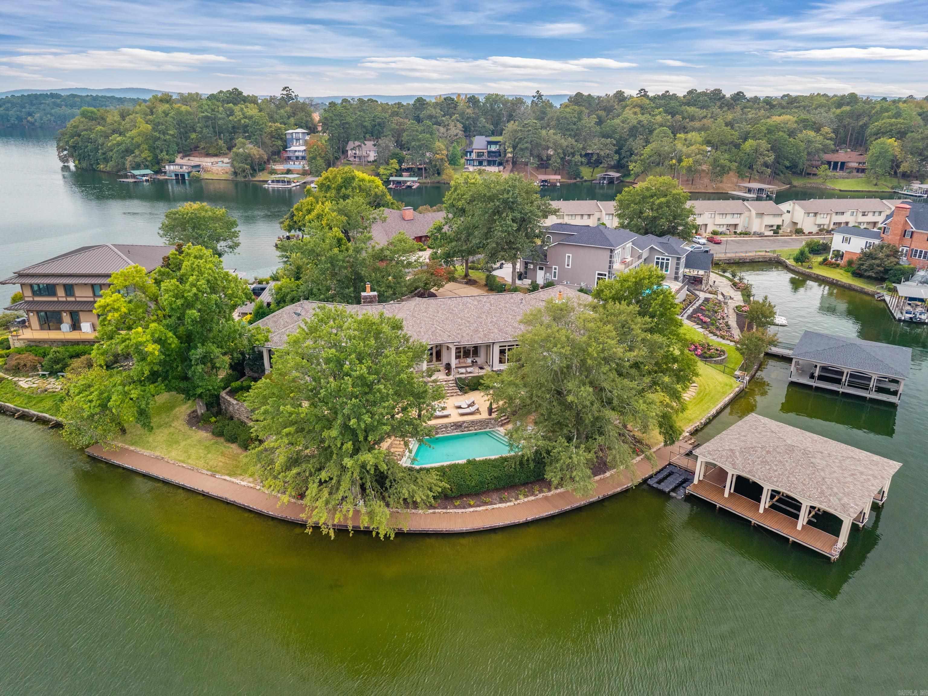 Exquisite Point Property on Lake Hamilton! Welcome to your private paradise on the shores of beautiful Lake Hamilton! This stunning one-level estate is perfectly positioned on an exclusive point offering 289 feet of pristine waterfront and panoramic lake views from nearly every room. Designed for both relaxation and entertaining, this home features an in-ground pool, multiple covered patios, and a private boardwalk with Trex decking leading to a 2-stall stationary boat dock complete with Sea-Doo slips. Inside, you’ll find a spacious open-concept layout boasting 3 bedrooms—each with a private ensuite, 3.5 baths, a dedicated office, and a game room/bunkroom perfect for kids or guests. The chef’s kitchen is a showstopper with stainless appliances, solid surface countertops, ample storage and pantry. Home also features a wet bar, and a temperature-controlled wine refrigerator.  Your primary suite offers the perfect retreat—complete with a spa-inspired bathroom and luxurious STEAM ROOM, creating a true sanctuary for rejuvenation. Additional highlights include hardwood floors, oversized  storage room in the unfinished basement, and encapsulated crawl space for peace of mind.