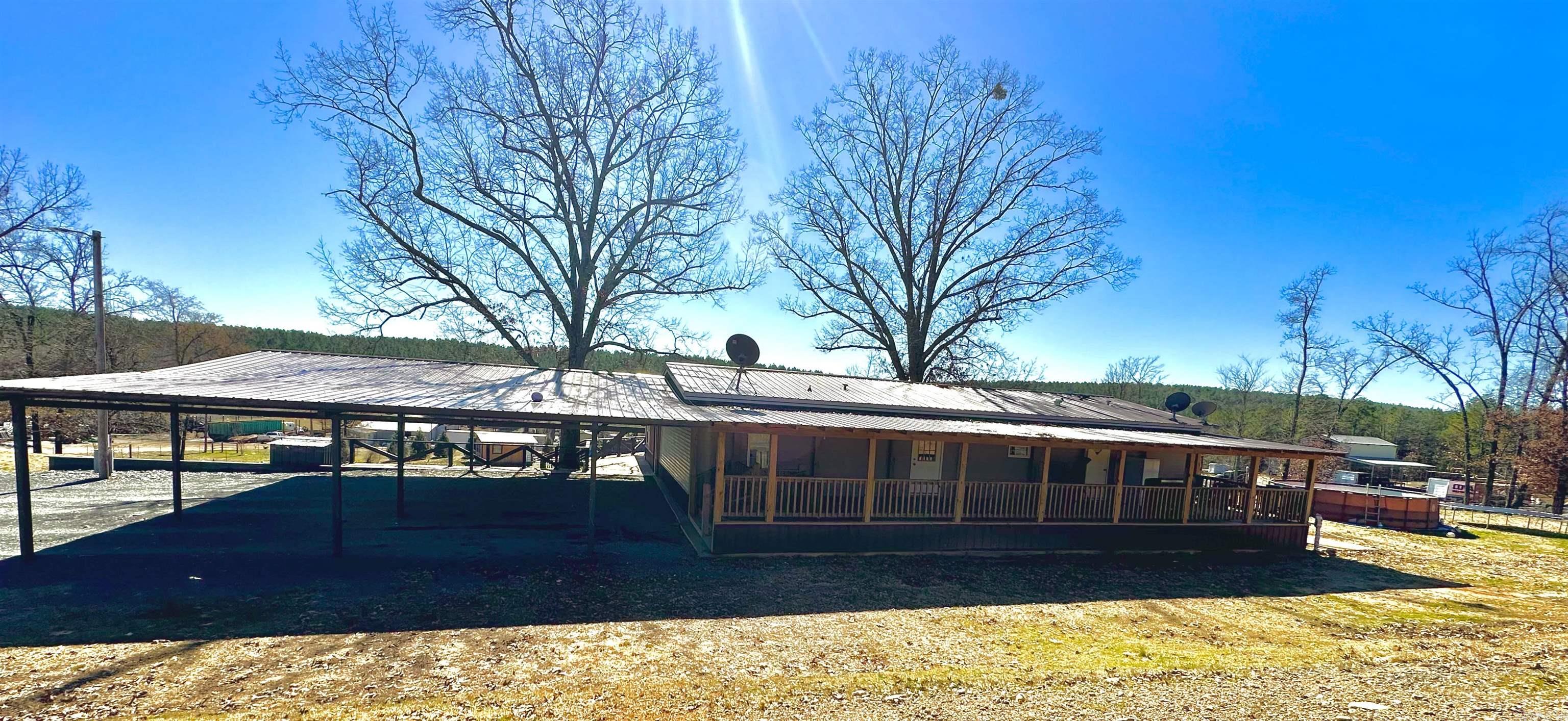 This 4 bed/2 bath doublewide sits on 3.5 acres m/l, is fenced all around, has a BEAUTIFUL 747 sq ft addition (outside completed, inside still needs work), a pond stocked with catfish, HUGE steel carport on the side, and an underground storage/storm shelter! NO RESTRICTIONS. The interior has an open kitchen/dining room with a large kitchen island, 3 bed/1 bath on one end and the primary bedroom is on the other end and has a walk-in closet and a big bathroom with a garden tub, some appliances/ furniture convey! The large front porch is the length of the home, has a ramp and steps, and has gates at both entrances/exits. VERY WELL BUILT. You can get to the MAGNIFICENT back deck that overlooks the backyard from 3 sides of the house. The stairs on the back deck lead to the backyard and underground storage/storm shelter. The house and porches are on a concrete slab! There is a well on the property, but it is currently running on city water. A big, fenced area in the back for a bountiful garden! There is an outbuilding with a lean-to in the back and a steel pen that sits on a concrete slab with two runs. It is just down the road from Cossatot High School.