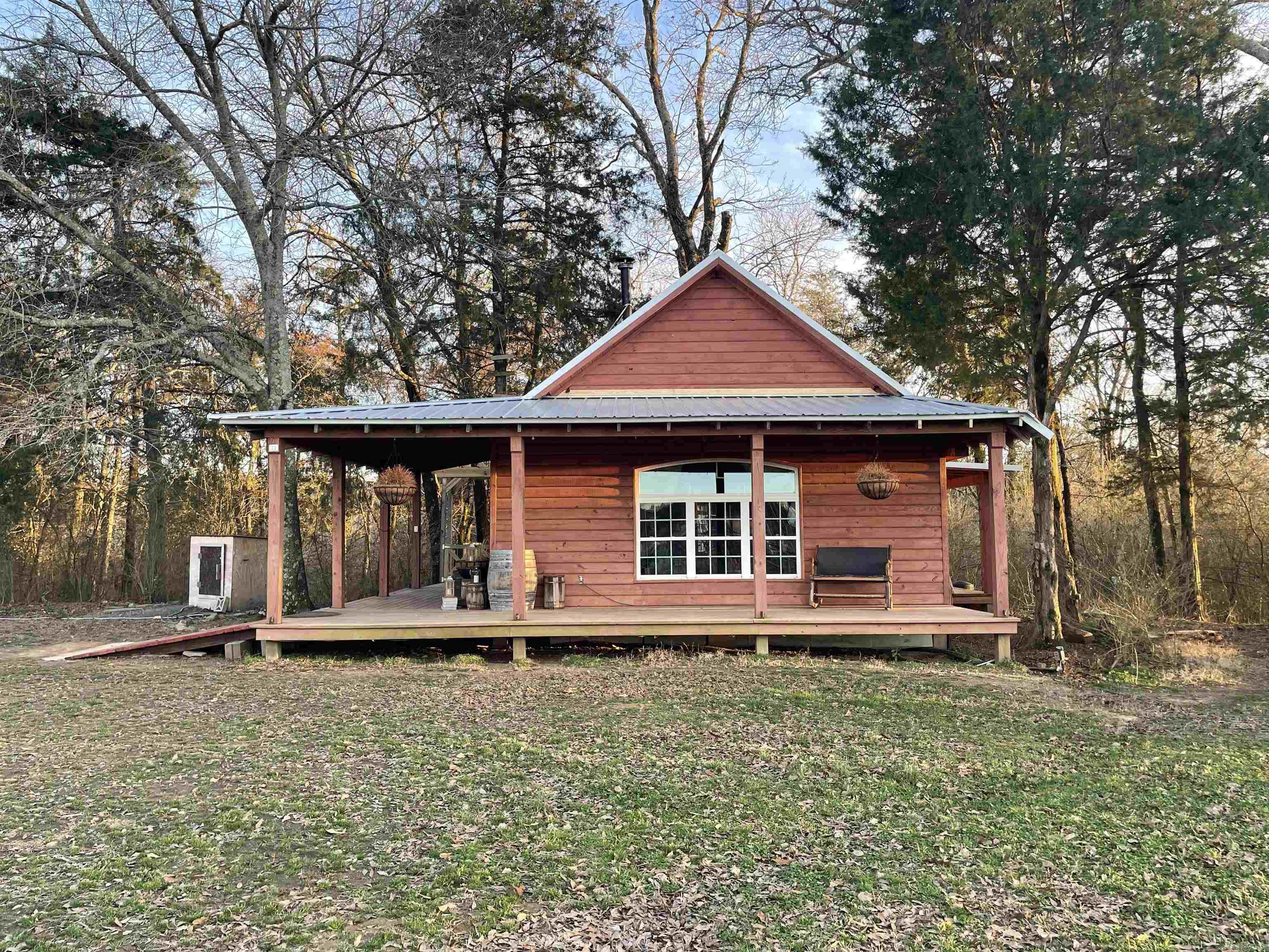 This warm, inviting log cabin sits on 50 peaceful acres near Mena, Arkansas, featuring vaulted ceilings, exposed beams, a large picture window, and a central wood stove anchoring the open living, kitchen, and dining area. It includes mini-split HVAC, private well, septic, and low taxes (under $300). A spacious 30x30 deck with pergola extends the living space outdoors.  The land offers year-round creek frontage on two sides, two ponds, pasture, mature timber, fencing, a shed, and a barn. Established orchards, berries, herbs, and 9 raised beds are supported by irrigation. Outbuildings with electricity provide space for office, guest, or studio use. Turnkey acreage with infrastructure already in place.