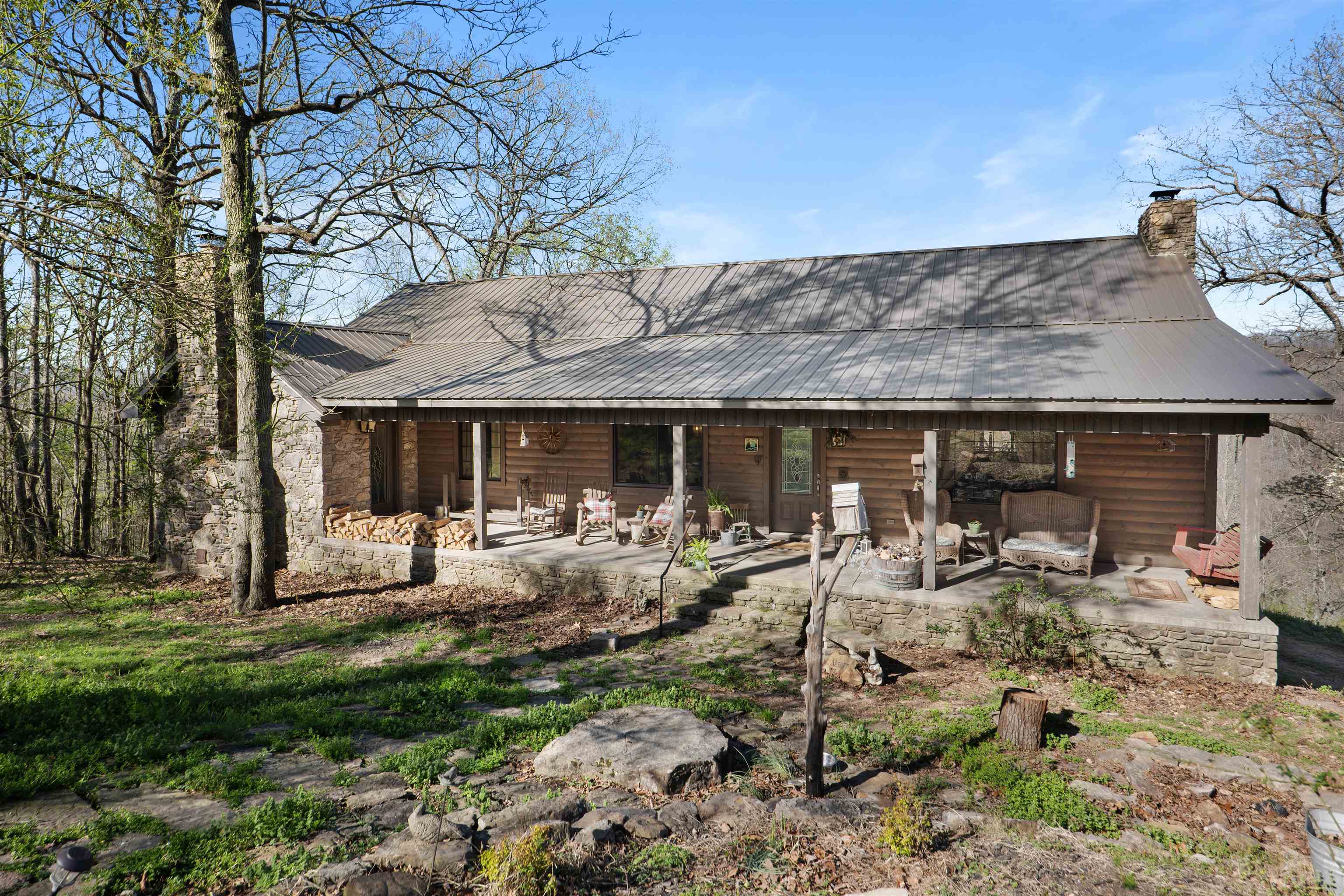 Tucked into the Ozarks, this log and native stone home has that true mountain feel from the moment you pull in. The main level offers 2 bedrooms and 2 bathrooms, with a finished walk-out basement featuring 2 flex rooms and an additional bath—perfect for guests, bunk space, or a second living area.  The living room centers around a beautiful native stone fireplace, with an additional wood-burning fireplace in the primary suite and a propane fireplace downstairs. The kitchen is built for gathering with granite countertops, oak cabinetry, and a commercial-style range with double ovens and griddle. Tall ceilings throughout add to the open, comfortable feel.  Enjoy the peaceful setting from the covered porch, with seasonal glimpses toward the Sylamore Creek Valley. Additional building with electric on a poured concrete foundation. Located just 12 minutes to the Ozark Folk Center and 17 minutes to Blanchard Springs Caverns—making this a great full-time home, weekend getaway, or vacation rental opportunity.