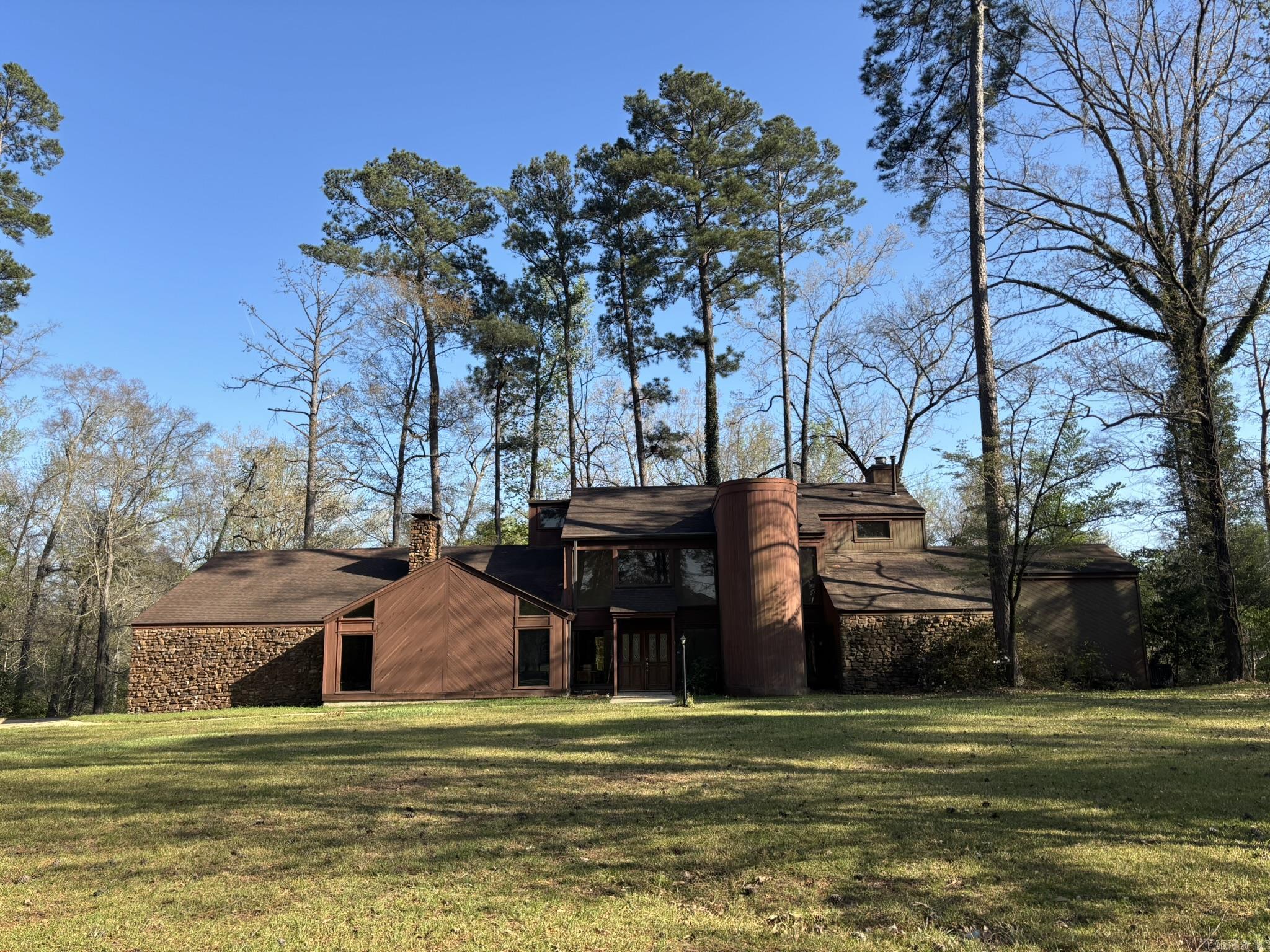 Nestled on a beautiful 5.8-acre wooded lot, this contemporary home offers privacy, space, & a prime central location. Inside, you’ll find two spacious family rooms – each featuring a fireplace, tongue-and-groove wood ceilings, exposed beams, & warm wood accents. The main living area boasts a soaring cathedral ceiling along w/ a built-in office space & bookcases. The 2nd living area offers tile flooring, a wet bar, & opens directly onto a large rear patio, perfect for entertaining. The main-floor primary suite features a generous walk-in closet & a private bath w/ dbl vanities, separate tub, & walk-in shower. Upstairs includes 4 bedrooms – several w/ lofts, plus a bonus room, floored attic, 1 full bath, & a Jack-and-Jill bath. The kitchen features vaulted ceilings & a dining area w/ windows overlooking the shaded lot, along w/ a separate formal dining space. Step outside to the rear deck & enjoy views of the in-ground pool, fire pit, & storage building. This home does need some TLC, offering a fantastic opportunity to make it your own & add value. *Being sold AS-IS WHERE-IS, NO REPAIRS. Pre-approval required. Square footage, lot size, and acreage is taken from courthouse records.