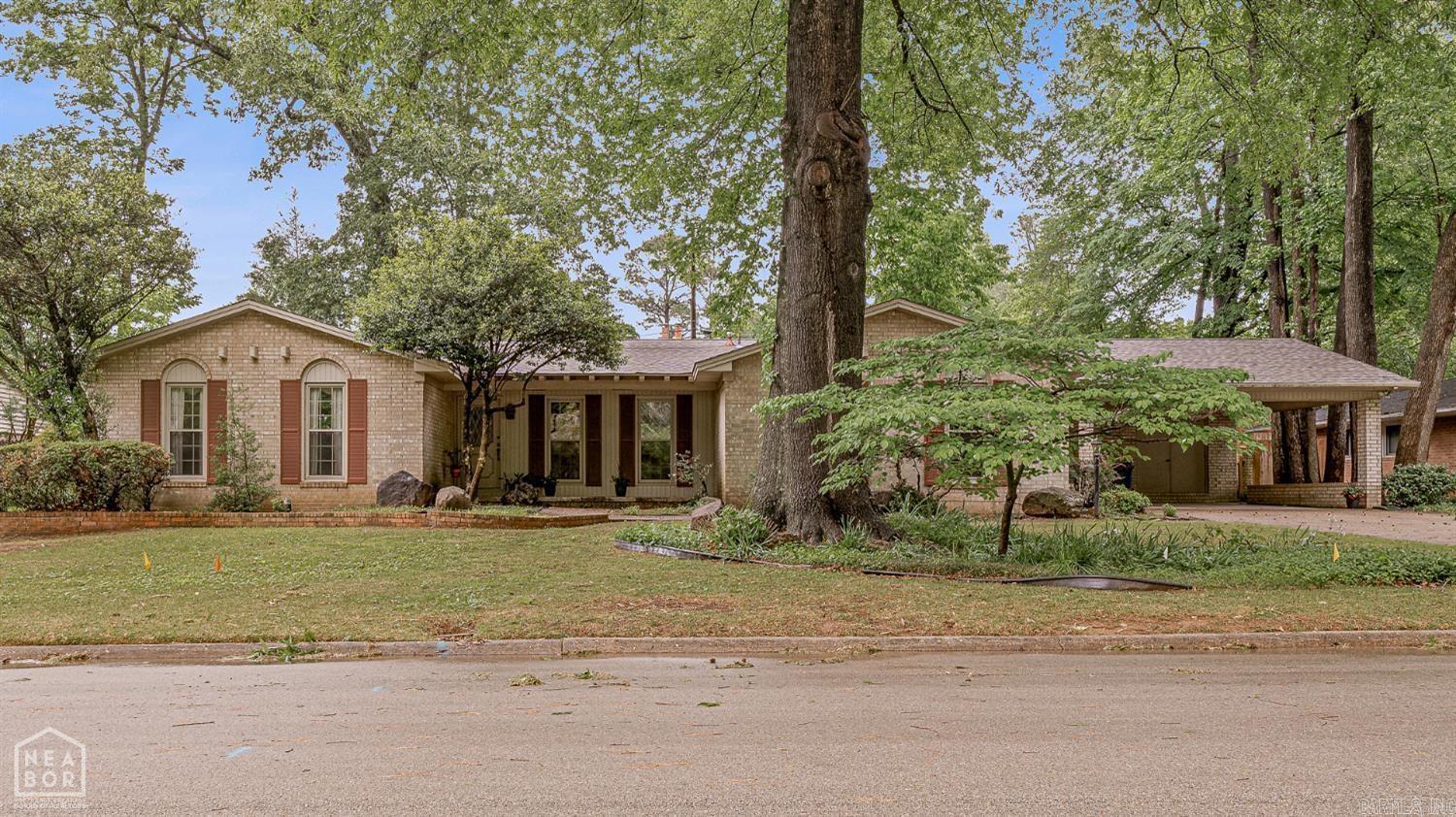 Nestled on a beautiful park-like setting with lush landscaping, this one-owner home offers charm, character, and room to make it your own. Built by Guy Pardew and lovingly cared for by its original owners, the home features a timeless brick exterior, a brand-new roof in 2026, and a carport large enough for two full-size vehicles, plus two large storage rooms. Inside, you'll find warm architectural details throughout, including arched entrances, vaulted ceilings, wood beam accents, and a gorgeous wood-trimmed room that could serve as a main living area, study, or library. The floor plan also includes a formal dining room, a kitchen with a brick accent wall, pantry, and a second living area with a gas fireplace. A smaller eating area off the kitchen would also make a great office or sitting space. The home offers three bedrooms, with two featuring ensuite bathrooms. The primary suite is tucked toward the back of the home and includes double closets, vaulted ceilings with wood beam accents, a stone wall, and private access to the backyard. Enjoy the peaceful setting from the screened-in back porch, surrounded by mature landscaping that truly feels like living in the middle of a park.