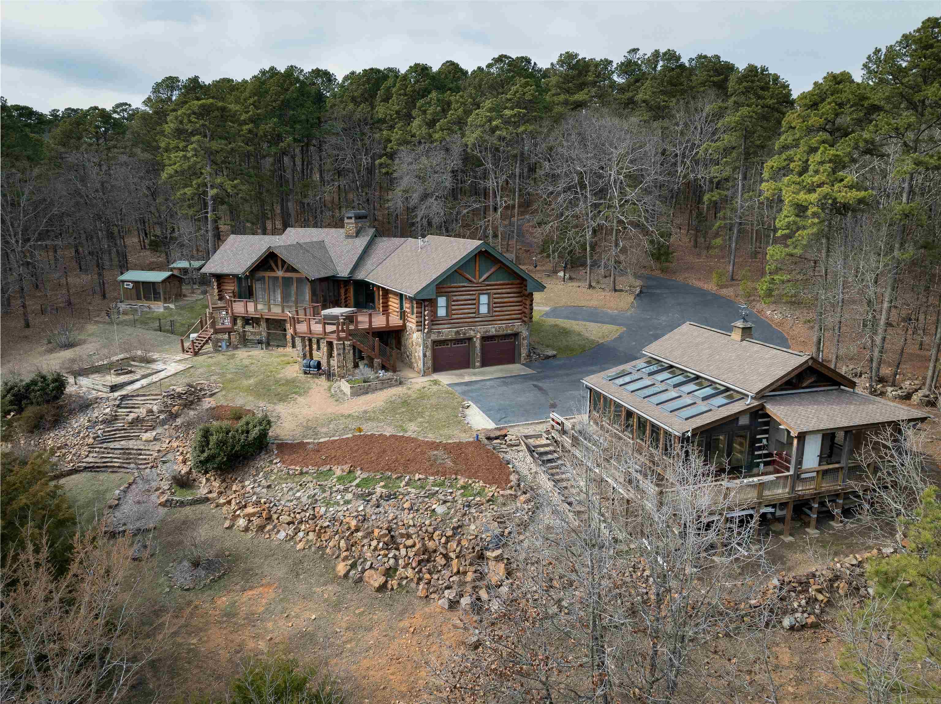 Have you always envisioned a cozy log cabin nestled among the trees? This rustic retreat in Roland sits on over 15 acres, offering a secluded haven surrounded by nature. The main residence boasts more than 3,500 square feet of living space, featuring three bedrooms and three full bathrooms for comfort and convenience. The heart of the home includes a double-sided stone fireplace, creating a warm and inviting atmosphere for relaxing or entertaining. The fully equipped kitchen  has granite countertops and a breakfast bar, perfect for casual dining and meal preparation. Enjoy your mornings with coffee on the deck or unwind in the screened-in porch while watching the stars in the evening. Beyond the main residence, the property features a large workshop that offers limitless possibilities for hobbies, projects, or storage.