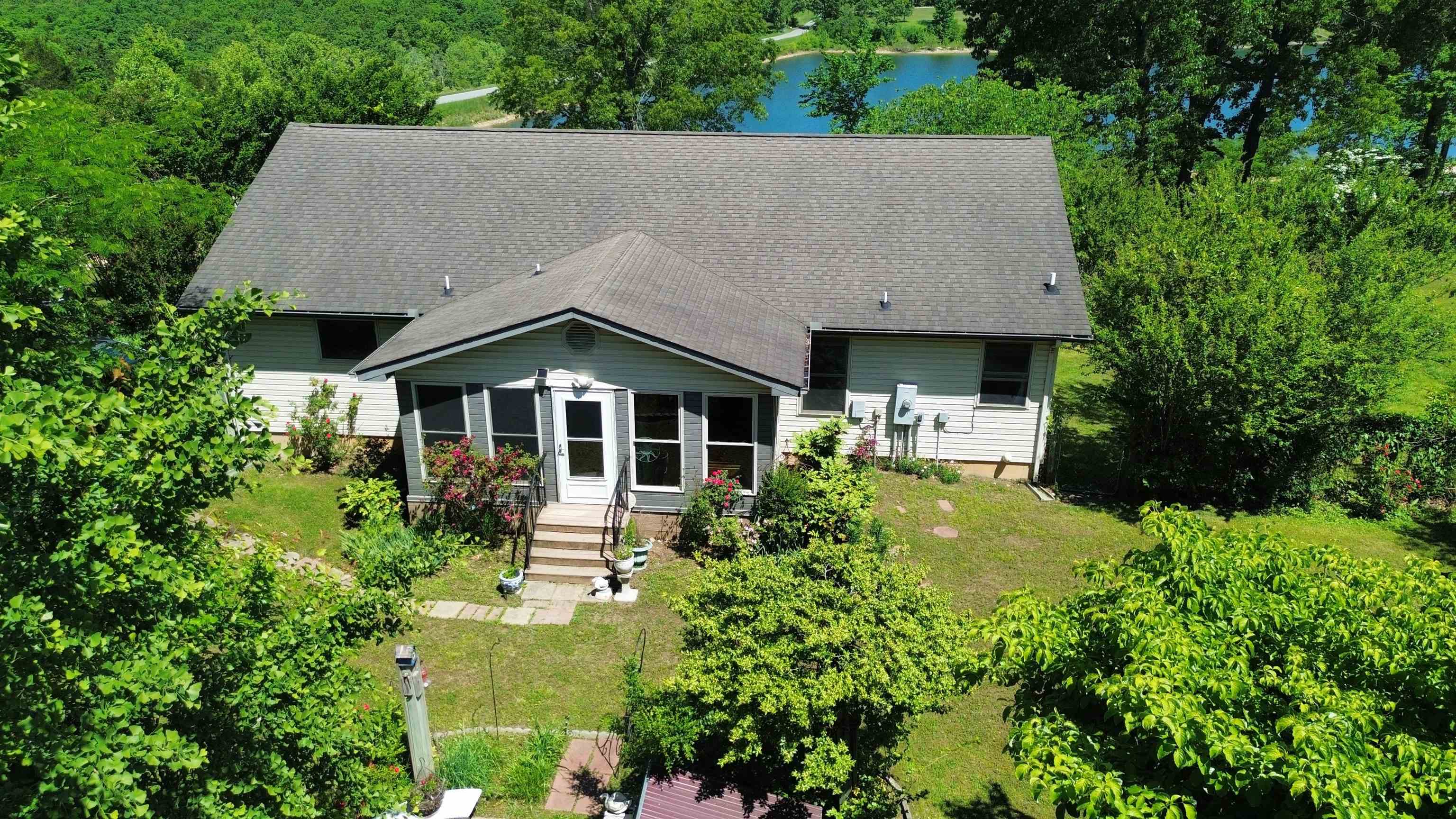 Lake views, peaceful surroundings, & room to truly enjoy the Ozark lifestyle—this 3 bed, 2 bath home offers over 3,200sqft with 1,600sqft upstairs & 1,600sqft downstairs, perfectly positioned across the street from Pioneer Lake. Spend your evenings fishing, kayaking, or walking to the beach for a swim just steps from your front door while still enjoying the privacy of rural residential living outside the city limits. The main level was designed for convenience with everything you need on one floor including the spacious primary suite with walk-in shower, laundry room, office space, & oversized utility/pantry area. The sunroom is overlooking a beautifully landscaped fenced in backyard filled with flowers, rose bushes, & garden charm—creating the perfect place for morning coffee or quiet evenings. Downstairs offers two additional bedrooms, a full bath, & a second living area ideal for guests, entertaining, or second living space. Large windows throughout the home capture natural light & peaceful lake views, while NEXT fiber optic internet keeps you connected. Additional features include a powered 1-car garage, extra storage, & the serenity front porch views of the Ozark foothills.