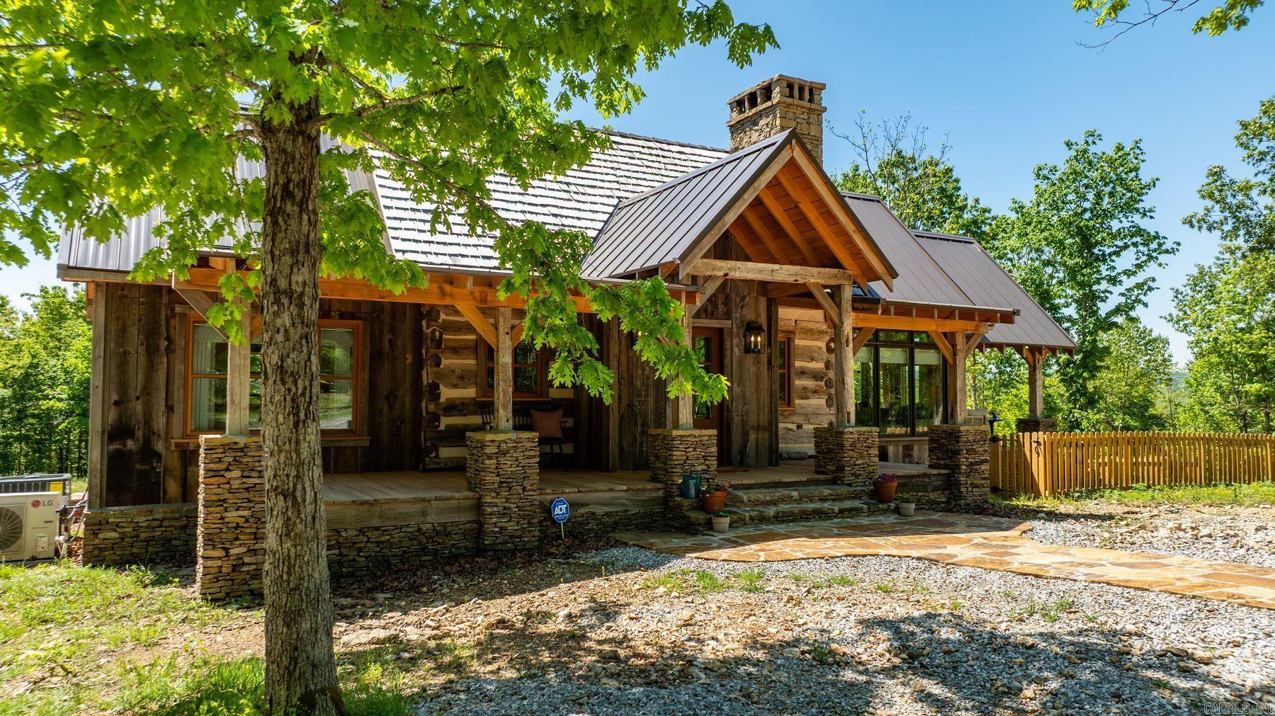 Set on 94 private acres in Timbo, From Off Farm is a rare blend of history, craftsmanship, and refined rural living. Centered around a nearly 200-year-old log cabin reassembled on site and expanded in 2023, this 4-bedroom, 2.5-bath home offers 1,380 square feet with three porches designed to take in the surrounding Ozark landscape. Authentic details define the home, including traditional chinking, mahogany casement windows, reclaimed wood flooring, and custom stained glass inspired by a Bear Paw quilt pattern. The kitchen features premium appliances, marble countertops, and custom cabinetry, while baths include soapstone and Moroccan zellige tile. The land offers two clearings, established trails, and a creek with rock bluffs. A 40x60 metal building with an efficiency apartment provides additional flexibility. Gated entry, storm shelter, private well, and abundant wildlife complete this exceptional, turnkey retreat.