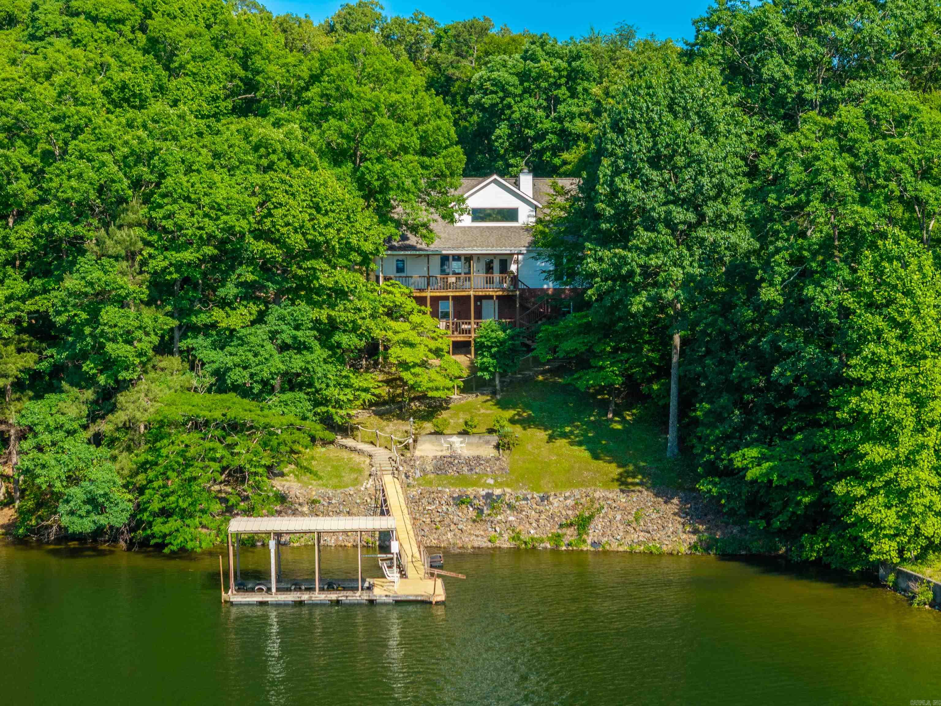 Welcome to 327 Longview Point — a truly rare opportunity on beautiful Lake Hamilton in Hot Springs, Arkansas. Nestled behind a private gated drive, this exceptional waterfront property offers over 5 wooded acres and approximately 400 feet of pristine shoreline with breathtaking full open-water views. This one-of-a-kind retreat features 3 bedrooms, 2.5 baths, and a dedicated office, combining comfort, privacy, and endless potential. The inviting living area is centered around a cozy fireplace and surrounded by stunning lake views, creating the perfect setting for relaxing or entertaining. The home also includes a basement area ideal for a workshop, storage, or future expansion. Enjoy direct access to Lake Hamilton with a one-stall covered floating boat dock. The private wooded setting offer sun matched seclusion while still being conveniently located in Hot Springs. With ample room for additional structures, guest homes, or future development, this property presents incredible possibilities for both personal enjoyment and investment potential. Properties like this rarely become available on Lake Hamilton. Investors take note — this is a legacy property with unlimited opportunity.