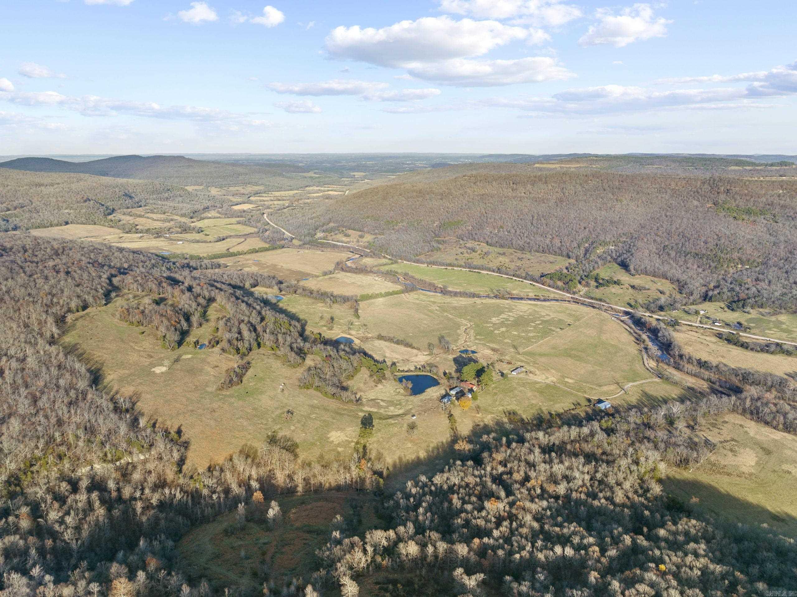 What an unbelievably rare and special tract on the famous Bear Creek. This stunning farm is loaded with features you just can’t duplicate and has something to offer any buyer. Tucked in the majestic valleys of this stretch of the Ozark Mountains is a rolling ranch with fantastic diversity. The massive and beautiful Bear Creek is flowing for over ¾ mile through the property. This year-round creek is known for its recreational perks; just imagine cooling off in the swimming holes on a hot summer day, hooking a smallmouth bass on a cool spring morning, sitting by the waterfalls listening to the soothing sound only running water can make, or even watching massive bull elk getting a drink on an early fall afternoon. Conveniently located on Hwy 27 South, the access is very easy and just a few miles from the community of Marshall, AR. The newly constructed masterpiece true log cabin is on one side of the road. This marvel is full of custom features like granite countertops, vaulted ceilings, custom alder doors, a towering freestanding dual-sided rock fireplace, an oversized covered wrap-around deck, custom hickory hardwood flooring, real wood blinds, and much more.