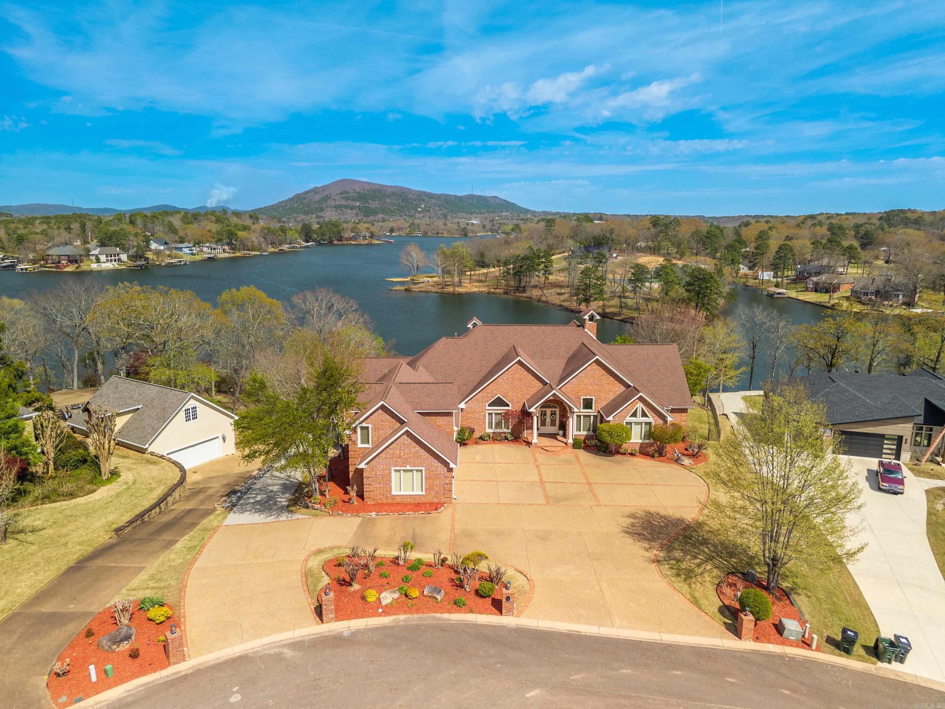 Experience refined lakefront living on Lake Hamilton with 248 feet of shoreline and 1.17 acres. This 6,008 sq. ft. home offers 4 bedrooms, 5.5 baths, and a versatile bonus room for a theater, studio, or guest space. Inside, soaring ceilings, floor-to-ceiling windows, and elegant architectural details create a bright, open setting anchored by a fireplace. The chef’s kitchen features an oversized refrigerator/freezer, wine fridge, ice maker, and generous prep space—perfect for entertaining.  Enjoy stunning lake and mountain views from the outdoor living area complete with a sparkling pool and fully equipped outdoor kitchen. A gentle path leads to a private two-stall covered boat dock for easy lake access. The primary suite offers expansive closets, a safe room, dual vanities, private water closets, and a spa-like bath with a custom open-air shower, jetted tub, and towel warmer.  Additional features include a large laundry room, workspace, butler’s pantry, plantation shutters, intercom, and central vacuum. Conveniently located near dining and shopping, yet privately tucked away, this home defines luxury lake living.