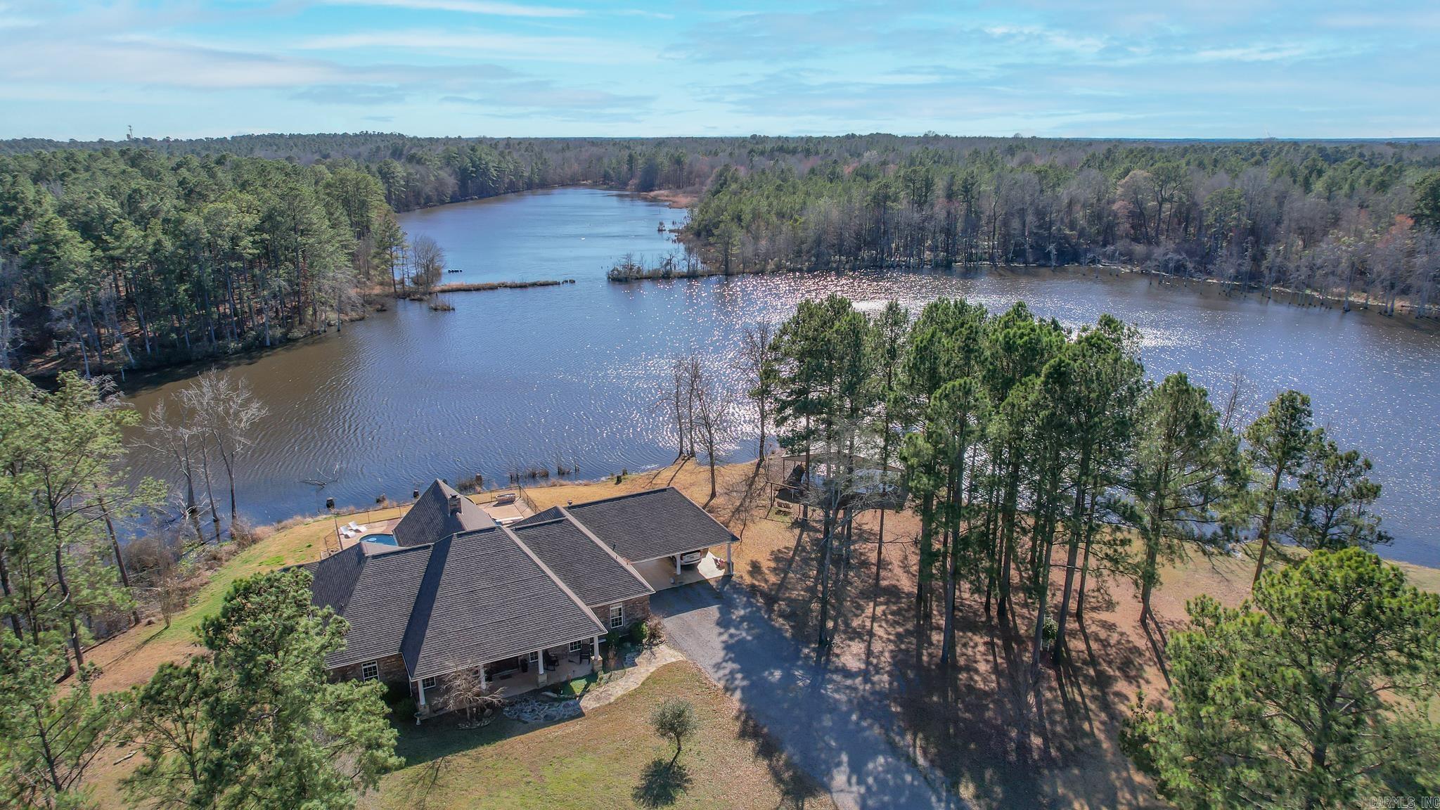 This unique property is a fisherman’s and outdoorsman’s paradise! Driving through the gate entry and winding down the long gravel driveway, you will find the house sits picturesquely and privately beside the lake creating breathtaking sunrises and sunsets, and incredible fishing opportunities! If bass fishing is high on your priority lists, then you don’t want to miss out on this one, properties such as this, don’t come along very often.  Improvements  The 3100 +/- SF three bedroom two and a half bath, home is well built with brick and stone construction, with a large kitchen complete with high-end appliances, a large master bedroom, and bathroom, as well as a stone fireplace in the living room. The interior finish has custom cabinets and molding, as well as tile and hardwood flooring throughout. A large front porch, two-car covered parking, and an incredible outdoor kitchen with a free form swimming pool compliment the outside of the home. Sitting on the back porch of the home and overlooking the lake is a site to see! The large storage/workshop is complete with HVAC, large overhanging porch areas, roll-up doors, and a great second kitchen/living area.
