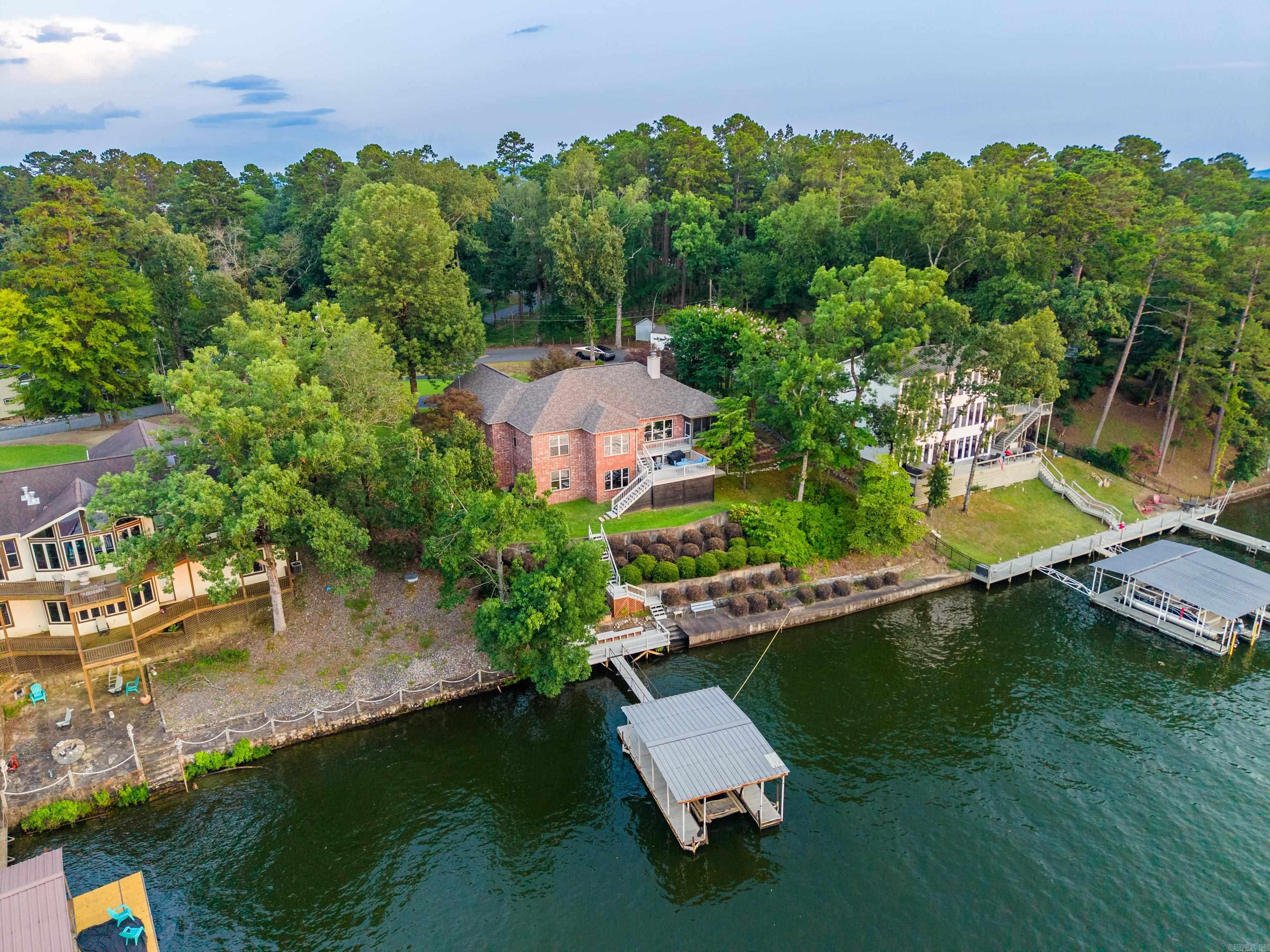 Lake Hamilton Living with Endless Possibilities! Wake up to breathtaking lake and mountain views from this impeccably maintained, custom-built waterfront home on Lake Hamilton. Lovingly cared for by its original owner, this one-of-a-kind property is nestled on approximately ¾ of an acre with year-round water frontage, offering the perfect blend of privacy, functionality, and everyday lake living. Designed with both comfort and flexibility in mind, the main level features 3 spacious bedrooms, 2.5 baths, beautiful custom hardwood flooring, and a warm, inviting fireplace that anchors the open living space. Expansive windows frame picturesque lake views, creating a peaceful backdrop throughout the home. Downstairs, you'll find a versatile lower level that can easily adapt to your lifestyle. Whether you're dreaming of a 4th bedroom, media room, game room, home gym, craft studio, home office, or guest retreat, this flexible space is ready to fit your needs. Complete with a wet bar, half bath, and a dedicated workshop for woodworking or hobbies, it's an ideal setup for entertaining, multi-generational living, or pursuing your passions.