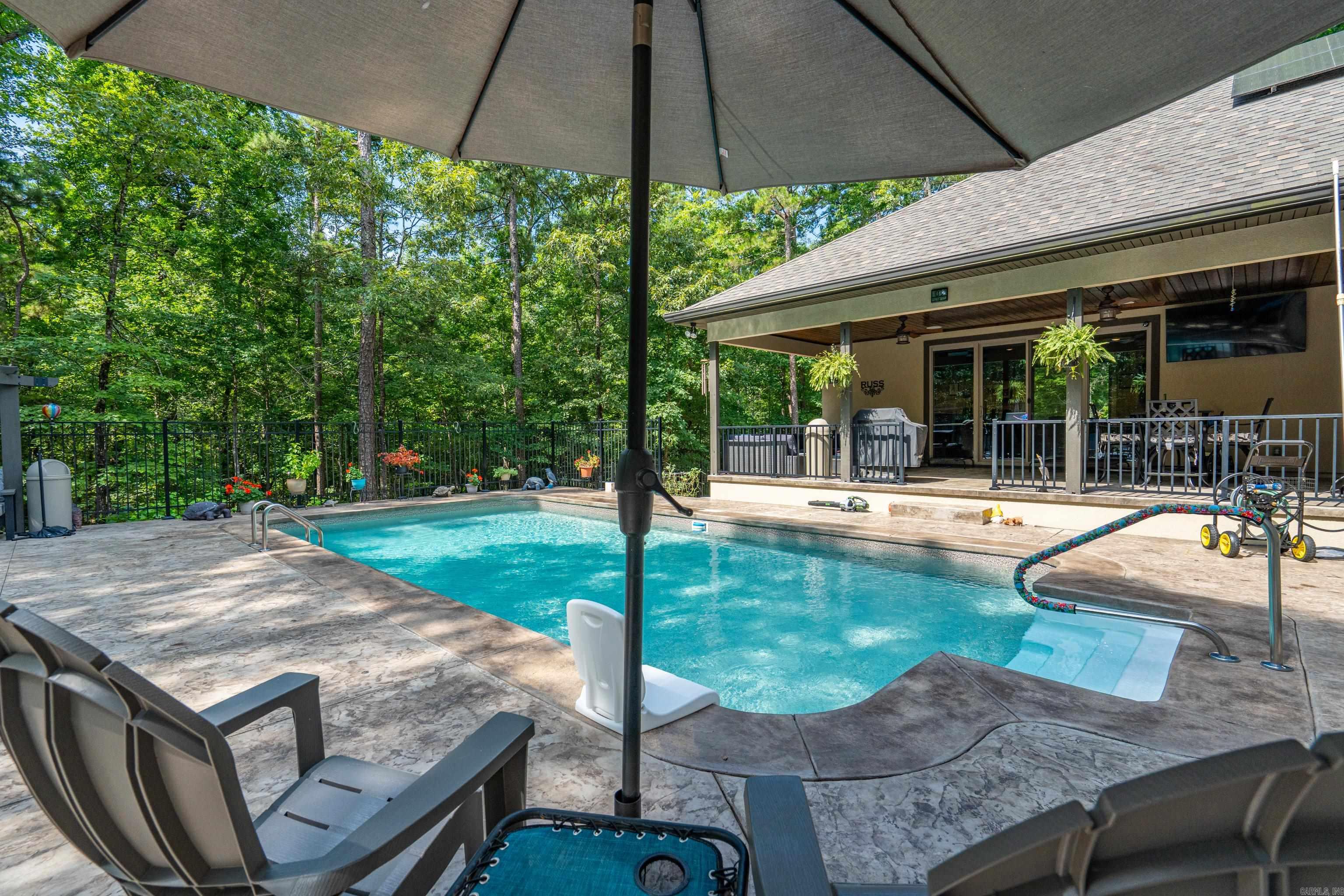 Private backyard oasis featuring a heated saltwater pool, pergola, stamped concrete patio, raised garden beds, and wrought iron fencing. This move-in ready home offers an open-concept floor plan designed for entertaining with a spacious living area, propane fireplace, and barn doors leading to an impressive game room complete with a custom bar, beverage fridge, icemaker, and built-in sound system. The primary suite is a true retreat with a spa-like bath featuring a walk-in shower, soaking tub, double vanities, private water closet, and oversized walk-in closet with direct access to the laundry room. Two guest bedrooms share a spacious bath with a walk-in shower. Enjoy resort-style outdoor living with a heated saltwater pool featuring an upgraded liner and dedicated heat pump for extended seasonal use. Relax under the pergola or entertain poolside in the beautifully landscaped backyard. Additional features include a 3-car garage with insulated doors, epoxy floors, ample storage, solar panels for energy efficiency, modern finishes, low-maintenance living, and a convenient location. A perfect blend of comfort, style, and functionality.