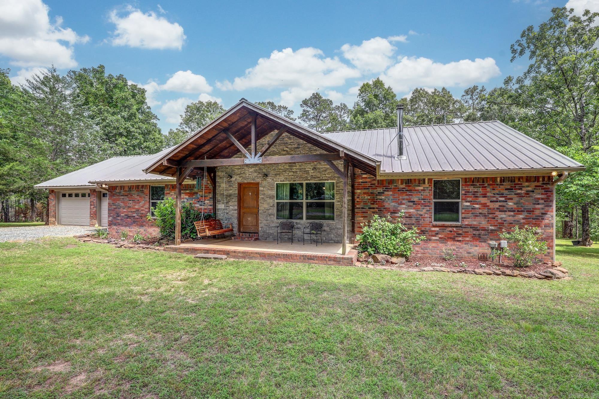 Tucked away at the end of a winding driveway, this one-of-a-kind custom home on 25 private acres offers the perfect blend of rustic elegance, craftsmanship, and peaceful country living. Built in 2012, this beautifully designed brick home welcomes stunning architectural details, soaring vaulted ceilings, and serene wooded views. The open-concept living area features striking stone archways, large windows that flood the home with natural light, and vaulted ceilings accented with oak wood that brings warmth and character to the space. The wall trim throughout the main living area and hallways are designed to mimic the appearance of a log-style retreat, creating a cozy yet refined atmosphere. A Franklin wood-burning stove serves as a beautiful focal point in the living room, perfect for relaxing evenings and gathering with family and friends. The kitchen combines functionality and style with custom hickory wood cabinetry, granite countertops, a center island, and stainless steel appliances. Engineered hickory flooring flows throughout the home, complementing the rustic finishes and custom craftsmanship found in every detail.