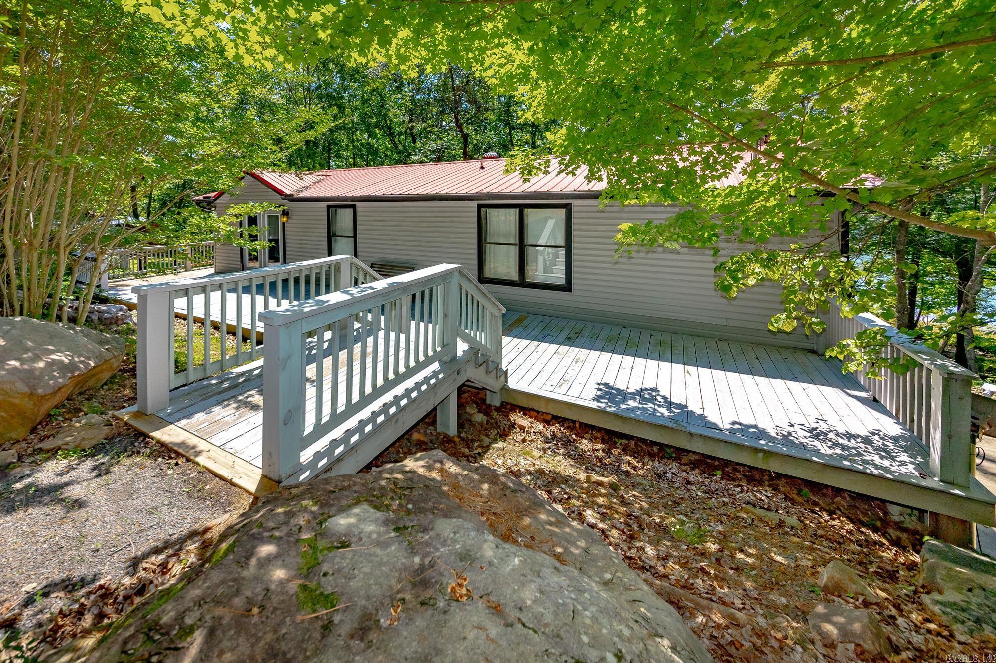 This lakefront opportunity does not come around often! Very very easy walk to the water from your back yard. Being able to have this view and easy walk is a very sought after thing around the Greers Ferry Lake area. Bring your clothes and toothbrush to this one and you are ready for your lake experience. All furnishings will stay to include bedding and even extra linens in every bedroom closet. Most artwork are one-of-a-kind pieces and bring a very tasteful decor to the home. There are 2 bedrooms on main level with one having an ensuite bath. Both bathrooms upstairs have jetted tubs. Downstairs you will find a kitchenette, open living space, and 2 more bedrooms and 1 bath. There are 5 outside doors downstairs. Each bedroom having their own door to outside. Safe room downstairs with access door from either inside or outside. Square footage measurement encouraged. A few photos/video have been AI modified or enhanced to show fire or sunset.