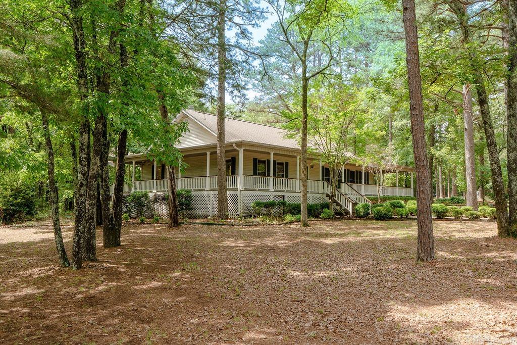 This spacious home sits on a beautiful 1.8-acre corner tract and welcomes you with a large wraparound porch perfect for relaxing and enjoying the peaceful setting. The 1,872 sq ft main level offers a split floor plan with a private primary suite separate from the guest bedroom. The primary ensuite features a new tiled walk-in shower, double vanity, and oversized walk-in closet. Fresh interior paint and new LVP flooring throughout the main level create a clean and updated feel, while the living room offers a cozy gas log fireplace. The kitchen is built for entertaining with a large island featuring a built-in gas range, plus a wet bar with ice maker. The dining room includes a full wall of built-ins for added storage. The finished basement adds a large game room or second living area, an additional bedroom, spacious safe room ideal for crafts or a workshop, plus fresh paint and new LVP in the living areas. Enjoy the peaceful wooded backdrop from the spacious deck. Attached 2-car garage plus an impressive heated/cooled 40x50 shop with shelving, 50-amp breaker, four 30-amp breakers, heated/cooled bonus room, chair lift, and motorized platform lift. Take a look!