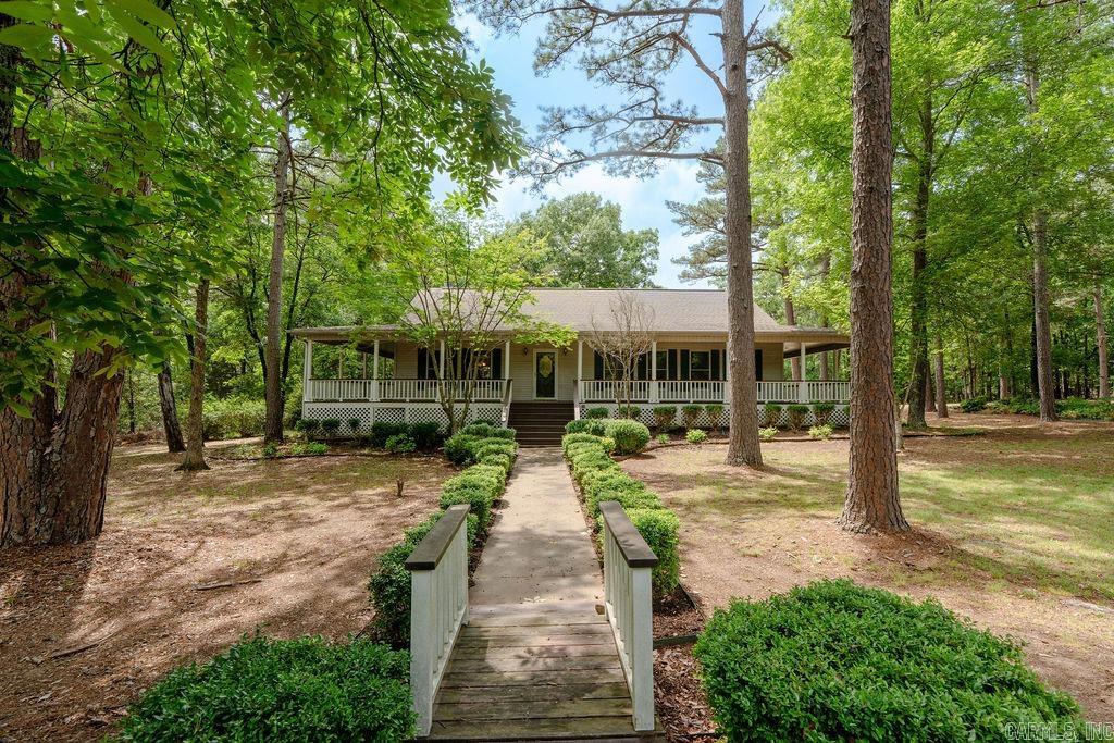 This spacious country-style home sits on a beautiful 1.8-acre corner tract and welcomes you with a large wraparound porch perfect for relaxing and enjoying the peaceful setting. The 1,872 sq ft main level offers a split floor plan with a private primary suite separate from the guest bedroom. The primary ensuite features a new tiled walk-in shower, double vanity, and oversized walk-in closet. Fresh interior paint and new LVP flooring throughout the main level create a clean and updated feel, while the living room offers a cozy gas log fireplace. The kitchen is built for entertaining with a large island featuring a built-in gas range, plus a wet bar with ice maker. The dining room includes a full wall of built-ins for added storage. The finished basement adds a large game room or second living area, an additional bedroom, spacious safe room ideal for crafts or a workshop, plus fresh paint and new LVP in the living areas. Enjoy the peaceful wooded backdrop from the spacious deck. Attached 2-car garage plus an impressive heated/cooled 40x50 shop with shelving, 50-amp breaker, four 30-amp breakers, heated/cooled bonus room, chair lift, and motorized platform lift. Take a look!