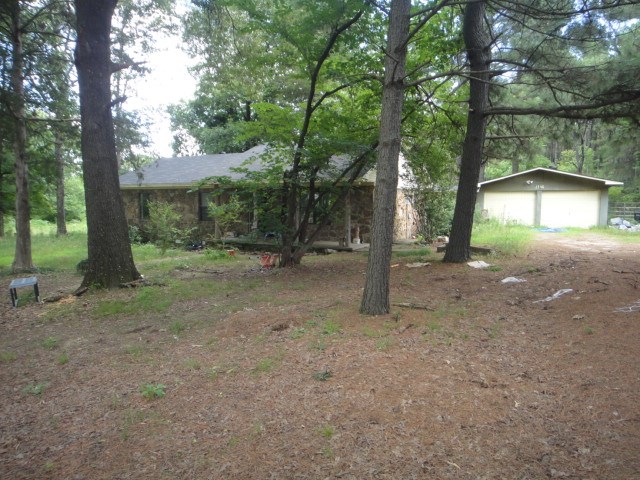 Enjoy a country setting in this rock home with large wooded acreage. Home has 3 BR/1.5 BA, Den with place for wood stove. Eat-in Kitchen. Sun porch, 2 car garage, Storm Shelter, Shed, partial wire fence. Great opportunity to increase value.  See Agent Remarks