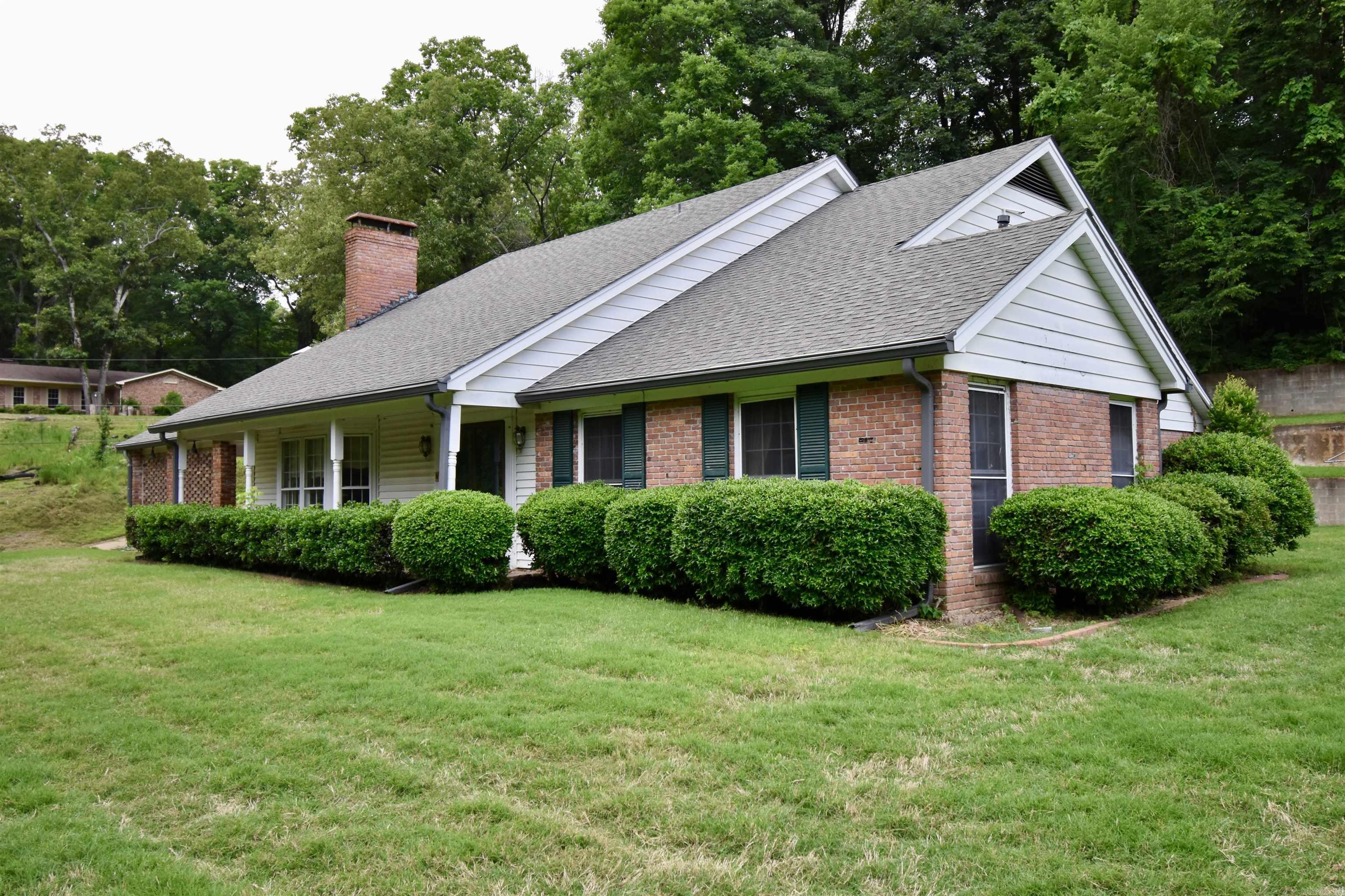 Nestled on approximately 3 private acres across three parcels, this spacious 3BR/3BA traditional home features beautiful outdoor space and a lighted tennis court on an adjoining lot. Surrounded by mature trees and a well-maintained lawn, the property provides a peaceful setting with convenient accessibility. The front entry opens to a striking staircase and formal living room featuring hardwood floors, a gas fireplace, and large windows with abundant natural light. The formal dining room flows into the kitchen, complete with double ovens, electric cooktop, island, breakfast area, decorative fireplace, dishwasher, garbage disposal, and access to a lovely back patio overlooking the property. An inviting den/hearth room includes exposed ceiling beams, a wood-burning fireplace, wet bar, bay window, and access to a covered carport with ample storage. The main-level primary suite features floor-length bay windows, built-in bookshelves, walk-in closet, and ensuite bath. Upstairs offers two bright bedrooms, shared full bath, and floored attic storage. Generator included. A rare opportunity to own a multi-parcel property with acreage, recreational amenities, and classic Southern charm.