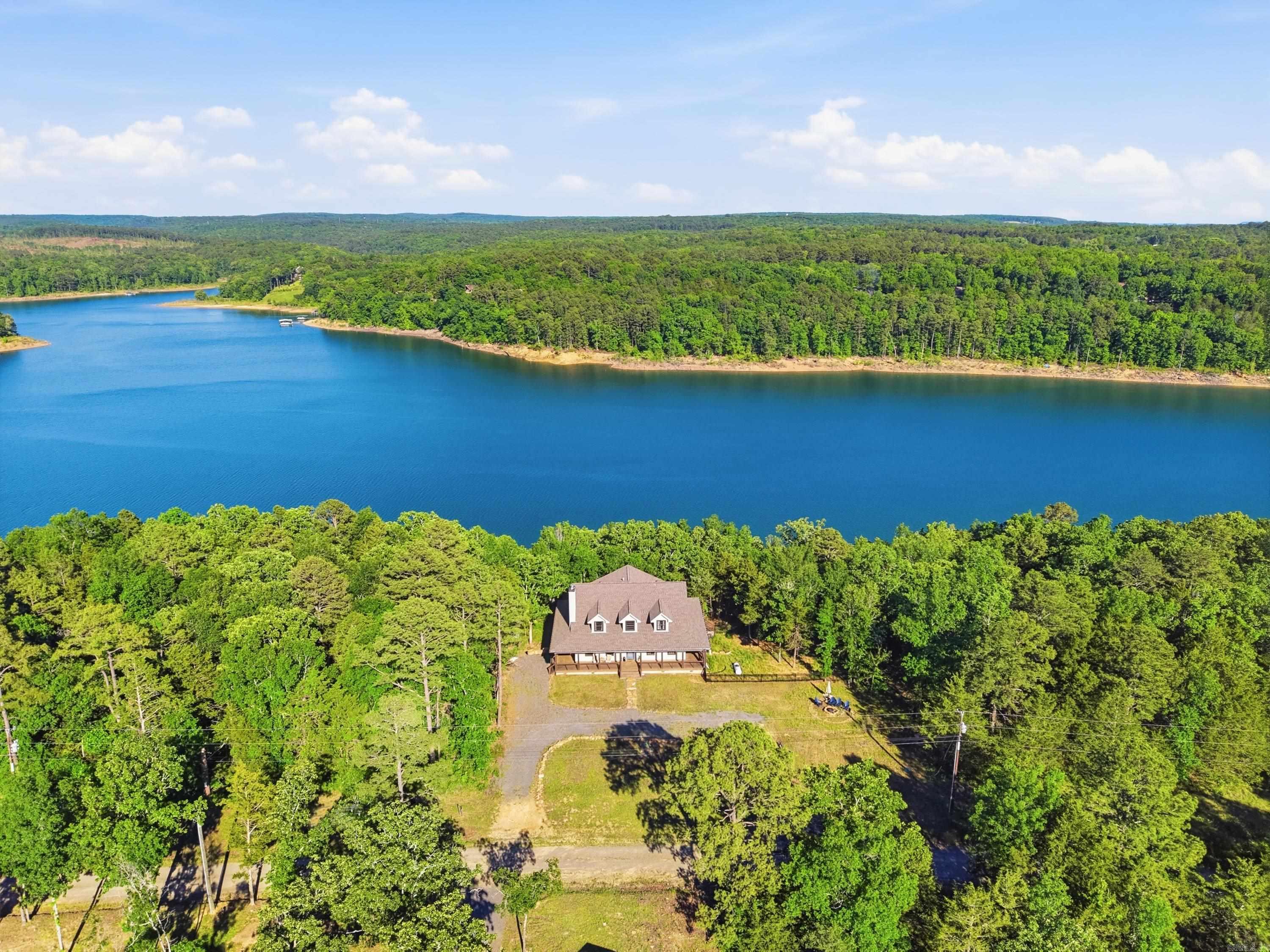 Experience luxury lake living at Greers Ferry Lake in this stunning 2024 custom-built home on a private half-acre wooded lot just steps from the water and only 200 yards from a public boat launch. This 3BR/3.5BA retreat features wraparound decks with panoramic views, a 30’ balcony with wet bar, custom rebar railings, and abundant outdoor entertaining space.  Inside, the open-concept great room showcases exposed beams, exposed brick, designer lighting, and a wood-burning fireplace. Each bedroom offers a spa-inspired en-suite with handcrafted cabinetry, deep soaking tubs, walk-in showers with double heads, infrared sauna, and private porch or balcony access. The downstairs primary suite includes heated floors and a remote-controlled bidet.  This home also features laundry rooms on each floor.  Bonus room upstairs can be used as a bedroom, office, library, or hobby room and has its own access to the balcony.  The gourmet kitchen features quartz countertops, a gas stove, wine cooler, and a handcrafted live-edge breakfast bar made from reclaimed barn wood. Additional highlights include an infrared sauna and ample storage throughout.