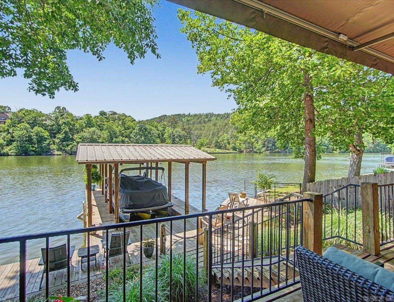 Nestled on the shores of Lake Hamilton, this beautifully designed 2-bedroom, 2-bath home offers the perfect blend of comfort, privacy, and lakefront living. From the moment you step inside, you’ll love the bright and airy feel created by soaring vaulted ceilings, 8-foot doors, and a stunning wall of windows that frames breathtaking water views and untouched National Forest property across the lake. Ceramic plank tile flows throughout the home, enhancing the clean, modern lake aesthetic while offering easy maintenance. The open living spaces feel cozy yet spacious, making this home ideal as a weekend retreat or full-time residence. Outside, enjoy a low-maintenance yard with lush landscaping, plus a fully fenced and gated setting designed for privacy and relaxation. An outdoor storage building provides plenty of room for all your lake toys and gear. With 53 feet of lake frontage, this property is built for enjoying life on the water. Features include a solid concrete seawall, a full-length boardwalk, a covered single-slip boat dock with swim platform, and 220 power ready for your boat lift, which conveys with the purchase. Tucked away on a quiet dead-end street in a quaint neighborho