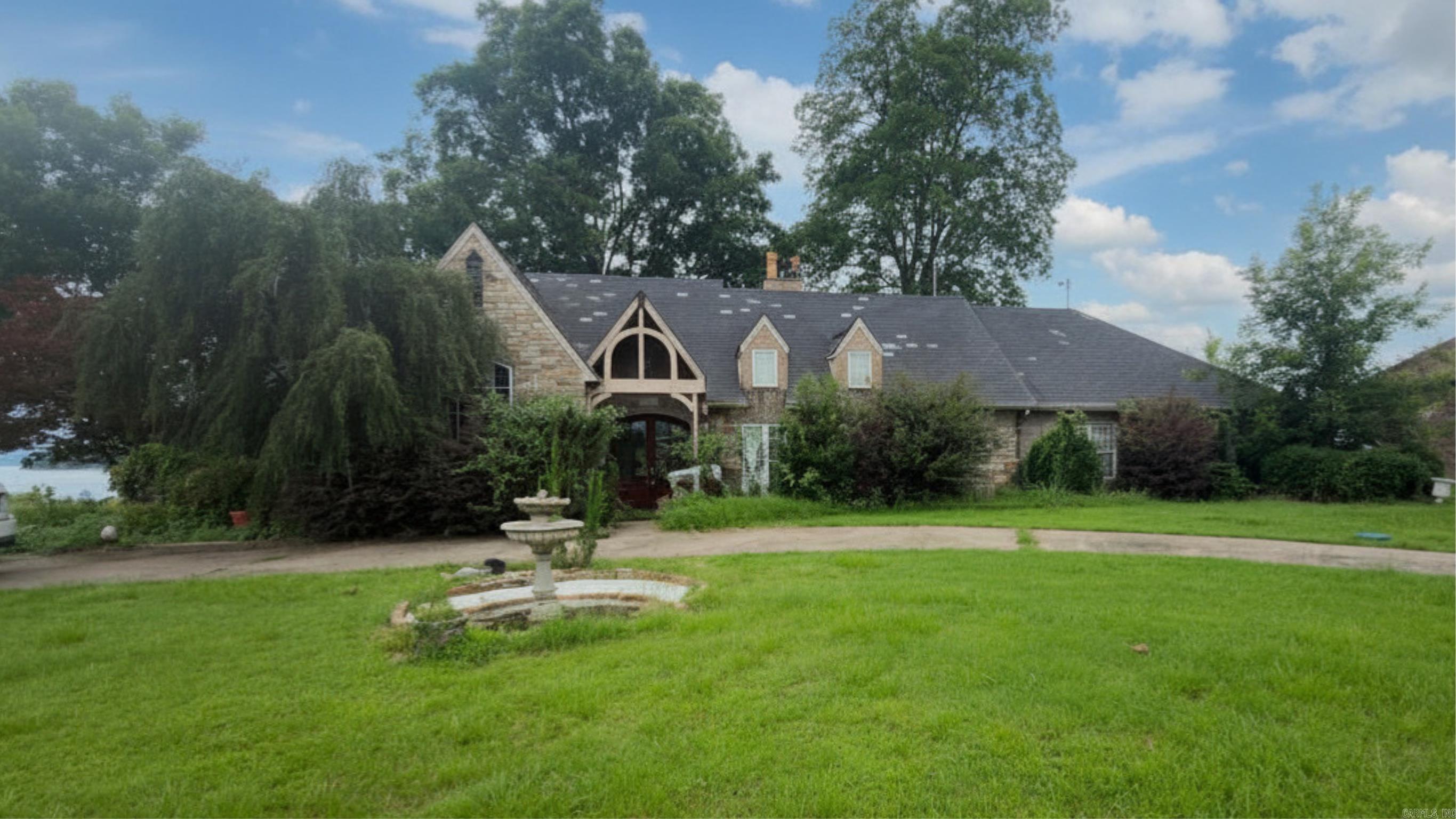 A rare opportunity to own a remarkable custom stone home directly on the Arkansas River! This one-level home makes a striking first impression with a circle drive and center fountain, a timber-framed gabled stone entry, and a screened front porch that adds a charming covered second entrance. Inside, the craftsmanship shines: soaring vaulted ceilings with exposed wood beams, a decorative ceiling medallion, rich hardwood floors, crown molding, arched built-in cabinetry, and tall Palladian windows. A fireplace anchors the family room, while walls of French doors frame sweeping river views and fill the home with light. The spacious kitchen features a dramatic floor-to-ceiling brick range alcove, a breakfast-bar peninsula, walk-in pantry, and a wall of windows over the water. Out back, a covered porch with a stone outdoor fireplace overlooks the lawn rolling down to private Arkansas River frontage—your front-row seat to unforgettable sunsets with Pinnacle Mountain on the horizon. This home needs TLC and is sold AS-IS as part of an estate (no property disclosure available)—a chance to restore this one-of-a-kind riverfront showplace and add equity. Bring your vision!