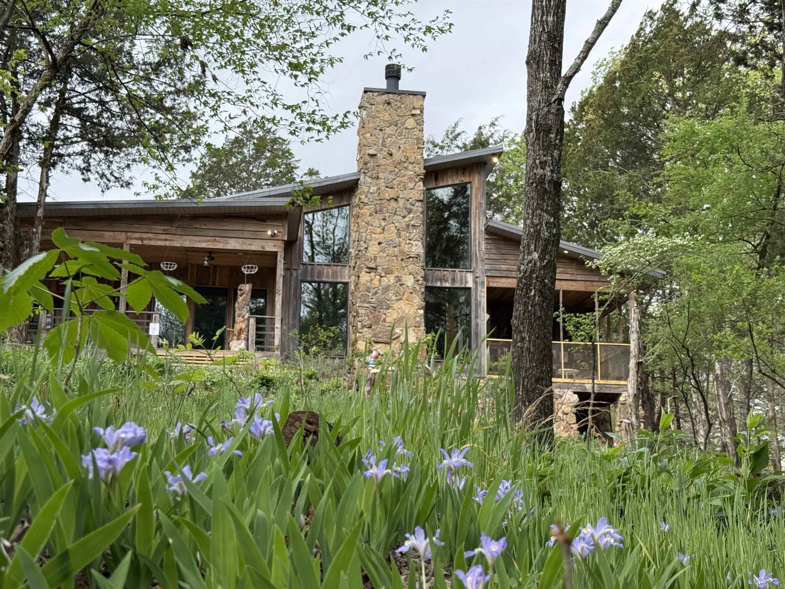 Absolutely stunning mid-century style lodge nestled in the middle of 5 private acres next to a gorgeous creek. You won't believe the peace and tranquility you'll find when you step into this home with 20' ceilings, open floor plan, natural light, gorgeous stone fireplace built with rock from White County, pine floors and beams all locally milled, all custom light fixtures from Poland and Slovenia, two living areas, custom kitchen cabinets and countertops with GE cafe appliances, and a loft for an office/playroom or music room. The primary suite features a custom tiled shower room, huge walk-in closet and a partially screened-in porch for sipping your coffee by the running water! The exterior is a mix of locally milled red and white oak. Other features include a spectacular mudroom, covered porches and don't forget the 30x40 shop with a separate wood-working room and steps leading upstairs to  1200 sq ft finished living space including a huge rec room with two bedrooms and a full bath all centrally heated & cooled. This stunning home was built with exceptional charm and intentional craftsmanship in every single room! Make your appointment to tour this breath-taking retreat today!