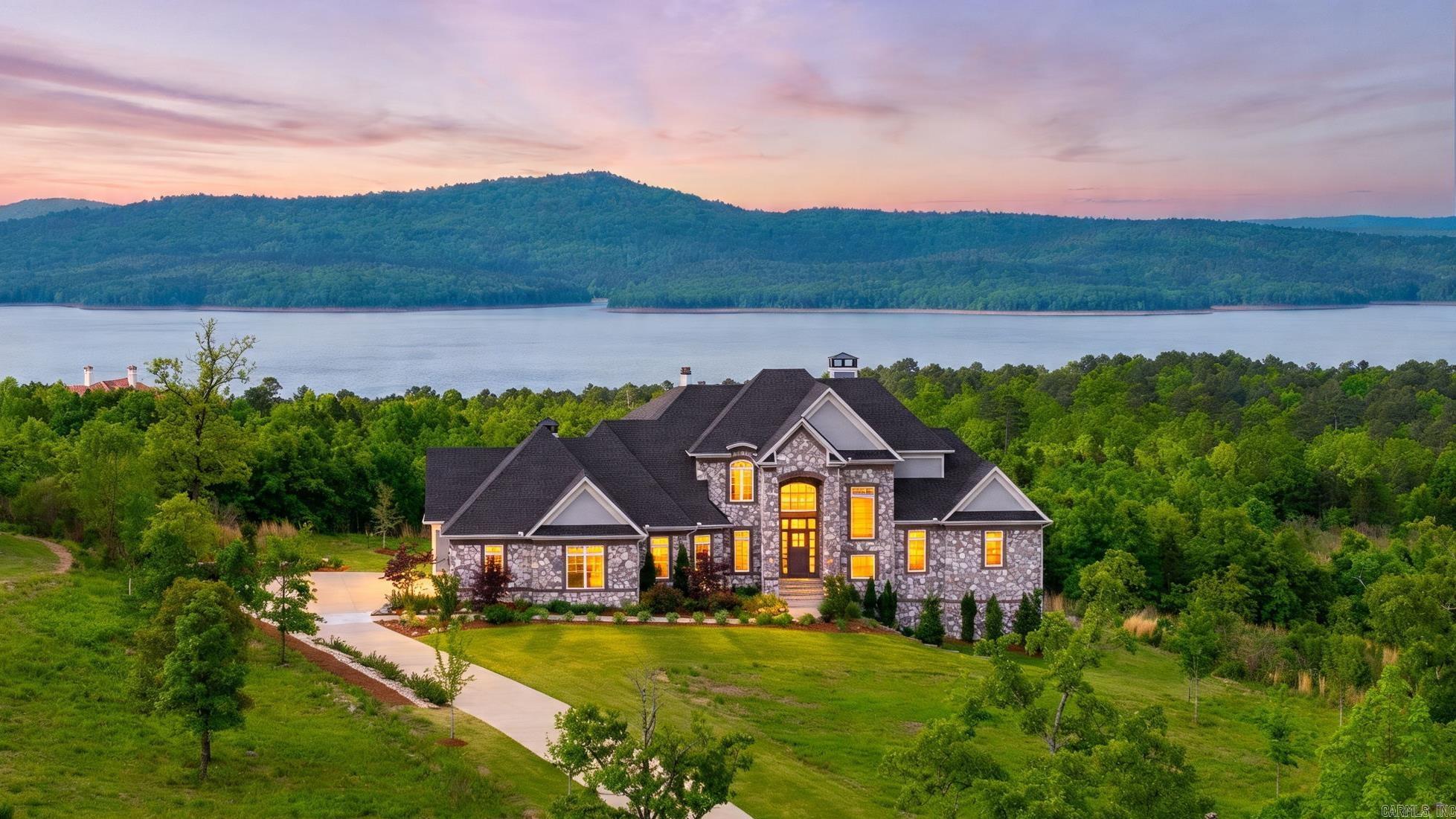 Incredible custom luxury home in gated Waterview Estates sits on over 1.6 acres with stunning views of Lake Maumelle. Impeccable landscaping creates a private, beautiful setting, perfectly complementing a home designed for everyday living, entertaining, and taking in the views. Natural light shines throughout, highlighting the chef’s kitchen with two islands, gas cooktop, upgraded appliances, and custom cabinetry. Enjoy a cozy sunroom with fireplace and patio access just off the kitchen. The two-story living room is a showstopper with floor to ceiling windows, a stone fireplace, and a striking staircase with custom iron railing. The main level also features a flexible sitting room or office, a serene primary suite with spa like bath (heated floors), half bath, laundry, mudroom, and oversized 3-car garage. Upstairs offers a bedroom with en-suite, an additional bedroom, full bath, and large bonus room. The walkout lower level is ideal for multi-generational living with a spacious living area, two bedrooms, and two full baths. Built in 2022 with energy-efficient features like tankless water heaters and zoned HVAC. Neighborhood amenities include trails, parks, sports courts and views.