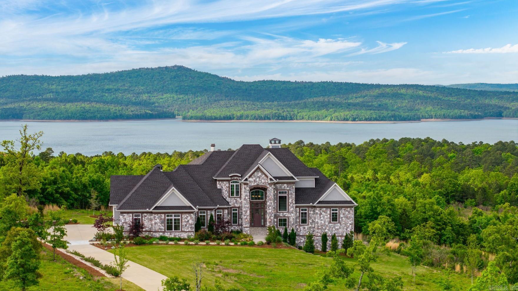 Incredible luxury home in gated Waterview Estates sits on over 1.6 acres with stunning views of Lake Maumelle. Impeccable landscaping creates a private, beautiful setting, complementing a home designed for everyday living, entertaining, and taking in the views. Natural light shines throughout, highlighting the chef’s kitchen with two islands, gas cooktop, upgraded appliances, and custom cabinetry. Enjoy a cozy sunroom with fireplace and patio access just off the kitchen. The two-story living room is a showstopper with floor to ceiling windows, a stone fireplace, and a striking staircase with custom iron railing. The main level also features a flexible sitting room or office, a serene primary suite with spa like bath (heated floors), half bath, laundry, mudroom, and oversized 3-car garage. Upstairs offers a bedroom with en-suite, an additional bedroom, full bath, and large bonus room. The walkout lower level is ideal for multi-generational living with a large living area, two bedrooms, and two full baths. Built in 2022 with energy-efficient features like tankless water heaters and zoned HVAC. Neighborhood amenities include trails, parks, sports court and views. Agents see remarks.