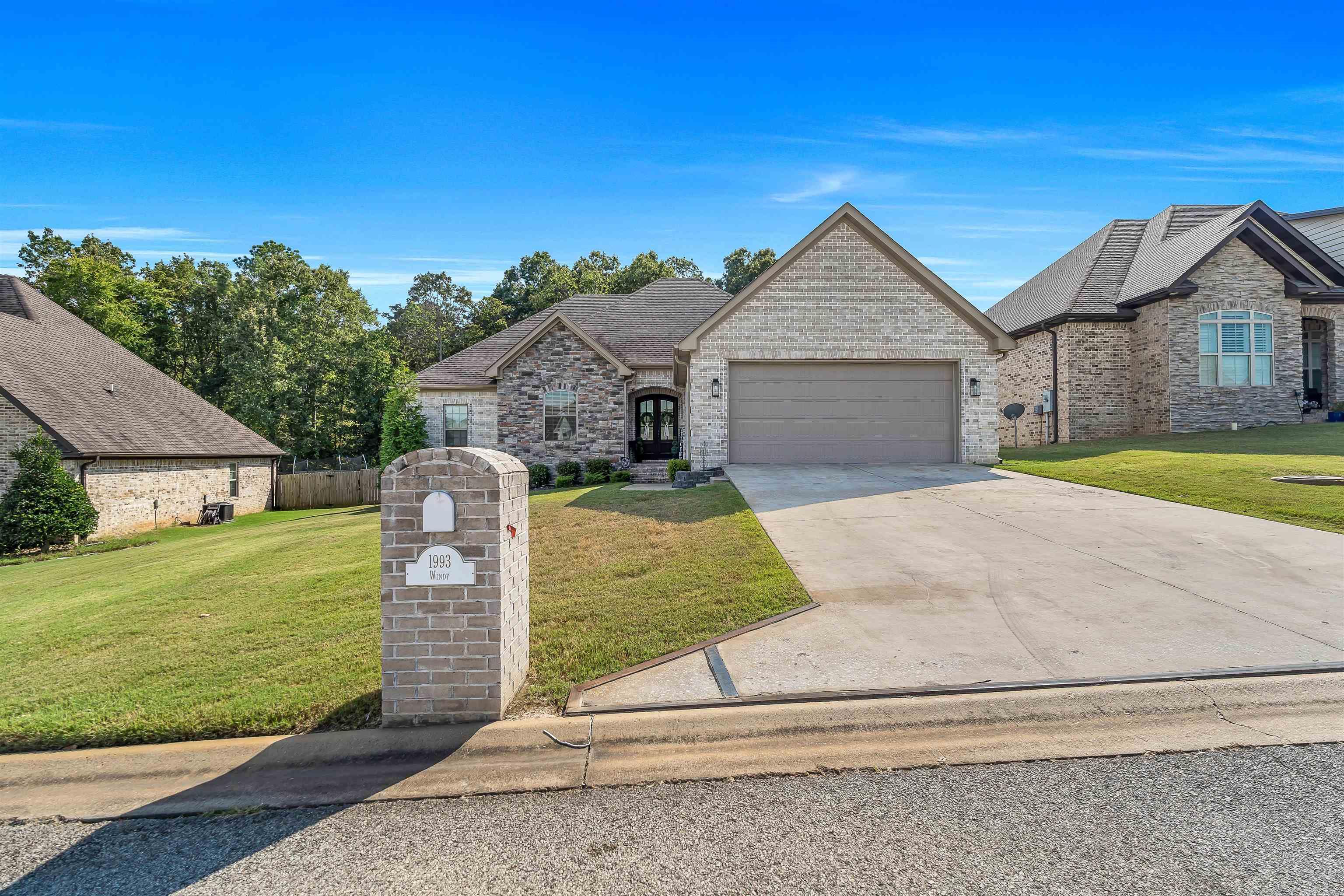 Welcome to 1993 Windy Lane, a stunning retreat in Jonesboro's desirable Valley View Manor. This thoughtfully designed stone-and-brick home offers 2,001 square feet of well-planned living space with a split floor plan featuring 4 bedrooms and 2.5 baths. Perched on an elevated lot, the home provides beautiful landscaping and peaceful, tree-lined views best enjoyed from the covered wood deck. Just minutes from Highway 49 South, you'll love the quick access to schools, shopping, and all of your favorite local amenities. The exterior showcases timeless curb appeal with a stone-and-brick facade, an architectural shingled roof, seamless gutters, a freshly sealed driveway, and a garage finished with epoxy flooring and urethane coating. Inside the garage, you'll find attic access, built-in storage, a storm-shelter system, and plenty of room for two full-size vehicles. Step inside through striking double mahogany doors with glass accents into a welcoming foyer. The living room impresses with soaring ceilings, wood floors, and a cozy fireplace that is perfect for Arkansas' cooler nights.