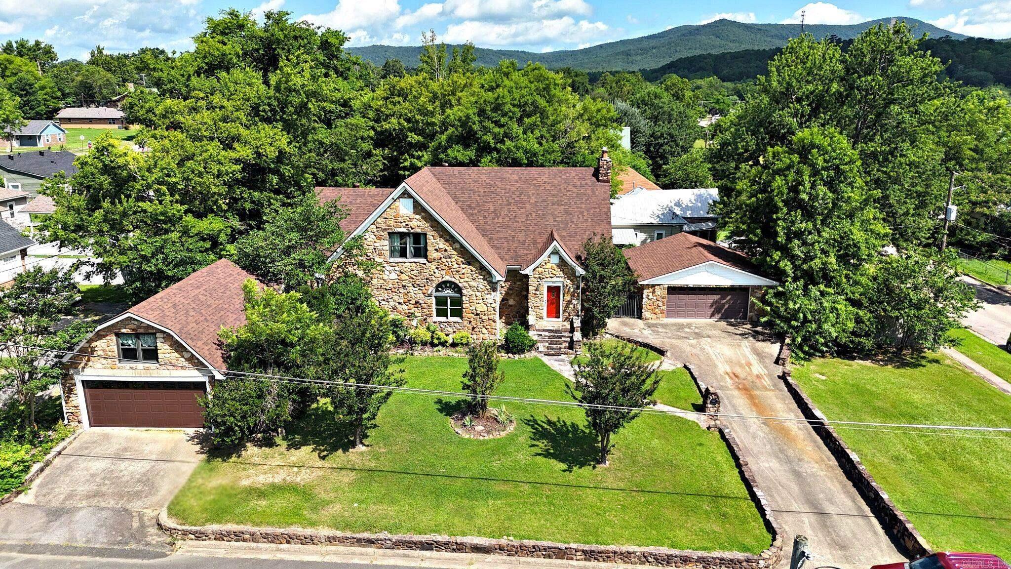 Overflowing with charm, this 4 BR/2 BTH, stone home on large corner lot offers approximately 2,926 sq/ft of living space and the kind of character that’s hard to find today. From the moment you arrive, the classic exterior, inviting front entry, and mature landscaping hint at the home’s longstanding place in the neighborhood. Inside, rich hardwood floors, a cozy fireplace, tall ceilings, and original built ins create warm gathering spaces that feel both gracious and welcoming. Vintage touches like the claw foot tub, checkerboard tile bath, detailed trim work, and arched window add a sense of historic significance and timeless style, while the spacious kitchen and multiple living and dining areas provide room to spread out and entertain. Home has 2 CH&A units. Outside, the expansive yard, paved drive, and detached garages complete this one of a kind property in a convenient in town location close to all Mena amenities. In the heart of Mena, this home puts you close to Ouachita Mountain hiking and ATV trails, Queen Wilhelmina State Park, Biking trails, local shops and restaurants, and small town community events.