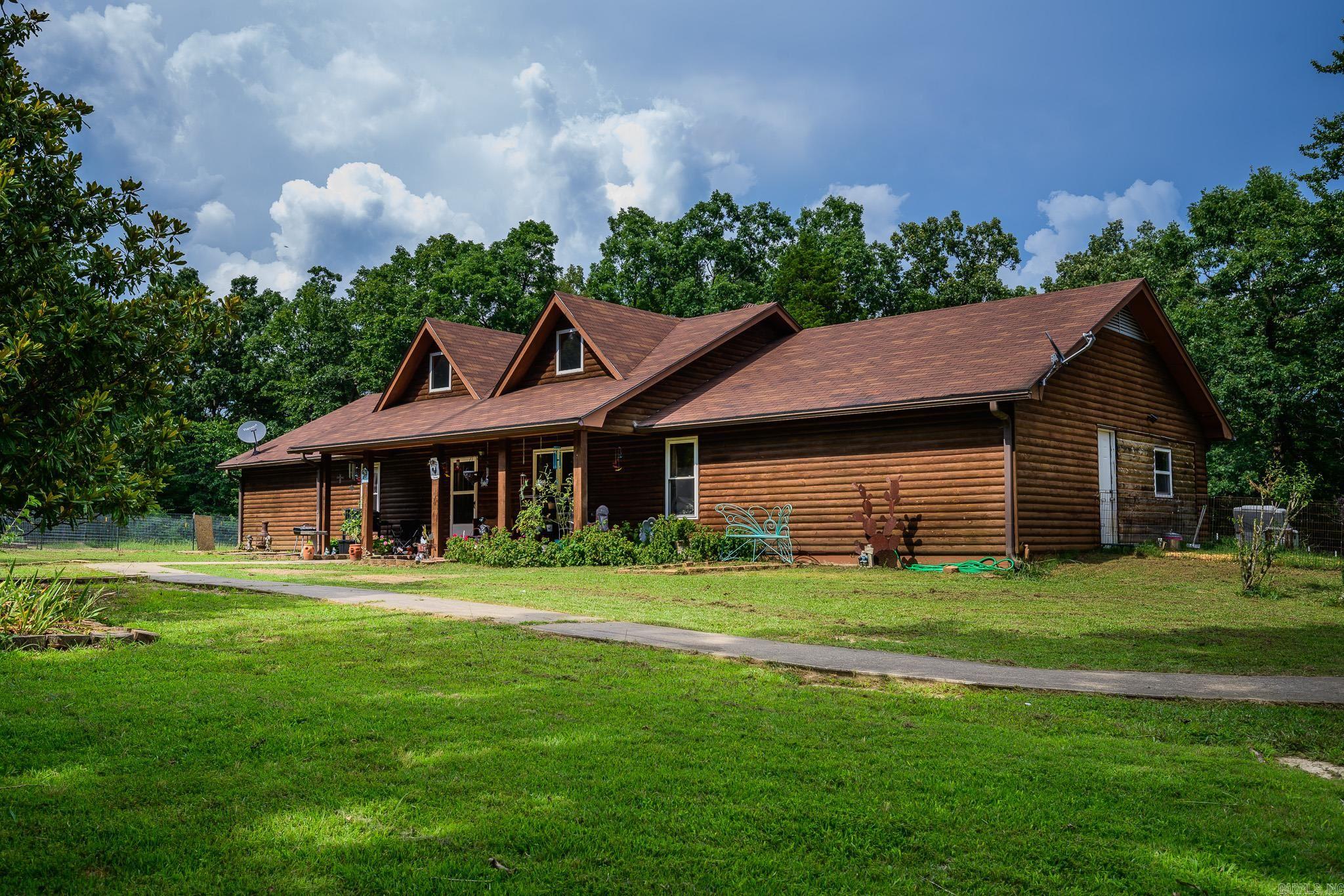 A beautiful log home nestled in a quiet subdivision just minutes from Mena, Arkansas. This property spans approximately 3.74 acres and is dotted with mature shade trees, offering both privacy and natural charm. The home is connected to public water, and the property also features three additional wells ideal for watering gardens, livestock, or landscaping. Outdoor storage is abundant—far more than a simple description can capture. Multiple outbuildings provide space for tools, equipment, and hobbies. Current structures include dedicated housing for chickens, geese, and ducks, plus a shop and an additional storage building; the shop and one outbuilding are equipped with electricity. Step inside to a welcoming living area with a vaulted ceiling. This spacious 4-bedroom, 2.5-bath home offers exceptional storage and room to spread out. The garage has been recently converted into a versatile space—perfect as a bedroom, game room, or in-law suite—complete with a half bath and a new mini-split A/C unit. Seasonal mountain views add to the charm, and sellers request a two-week delay of occupancy after closing. Agents see remarks.