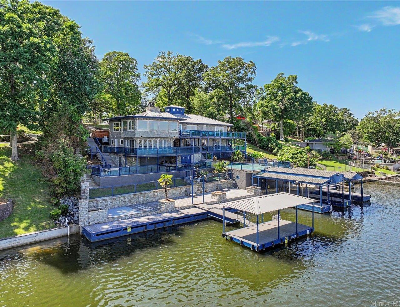 Experience Lake Hamilton living in highly desirable Moonlight Cove. This extensively updated waterfront home features custom craftsmanship, modern upgrades, and exceptional outdoor entertaining spaces. Highlights include authentic rock exterior, custom iron doors, luxury vinyl flooring, solid wood doors, skylights, decorative molding, and nautical-inspired details throughout.  The remodeled upper kitchen offers granite countertops, gas cooking, induction cooktop, pot filler, and like-new appliances; the lower level includes a second kitchen with Viking stove and multiple living areas ideal for guests or multigenerational living. Additional features include steam shower, 3 jetted tubs, fireplace, limestone accents, and expansive lake views.  Outdoor amenities include approx 10,000 SF of steel-framed decking, upgraded Garapa hardwood decking, gas hookups, custom lighting, covered swim dock, heavy-duty boat lift, and a fully equipped boathouse with full bath.  Recent updates include a 2025 standing seam metal roof, Pella windows and sliding doors, updated electrical and lighting, sprinkler system, alarm system, and downstairs fire sprinkler system.