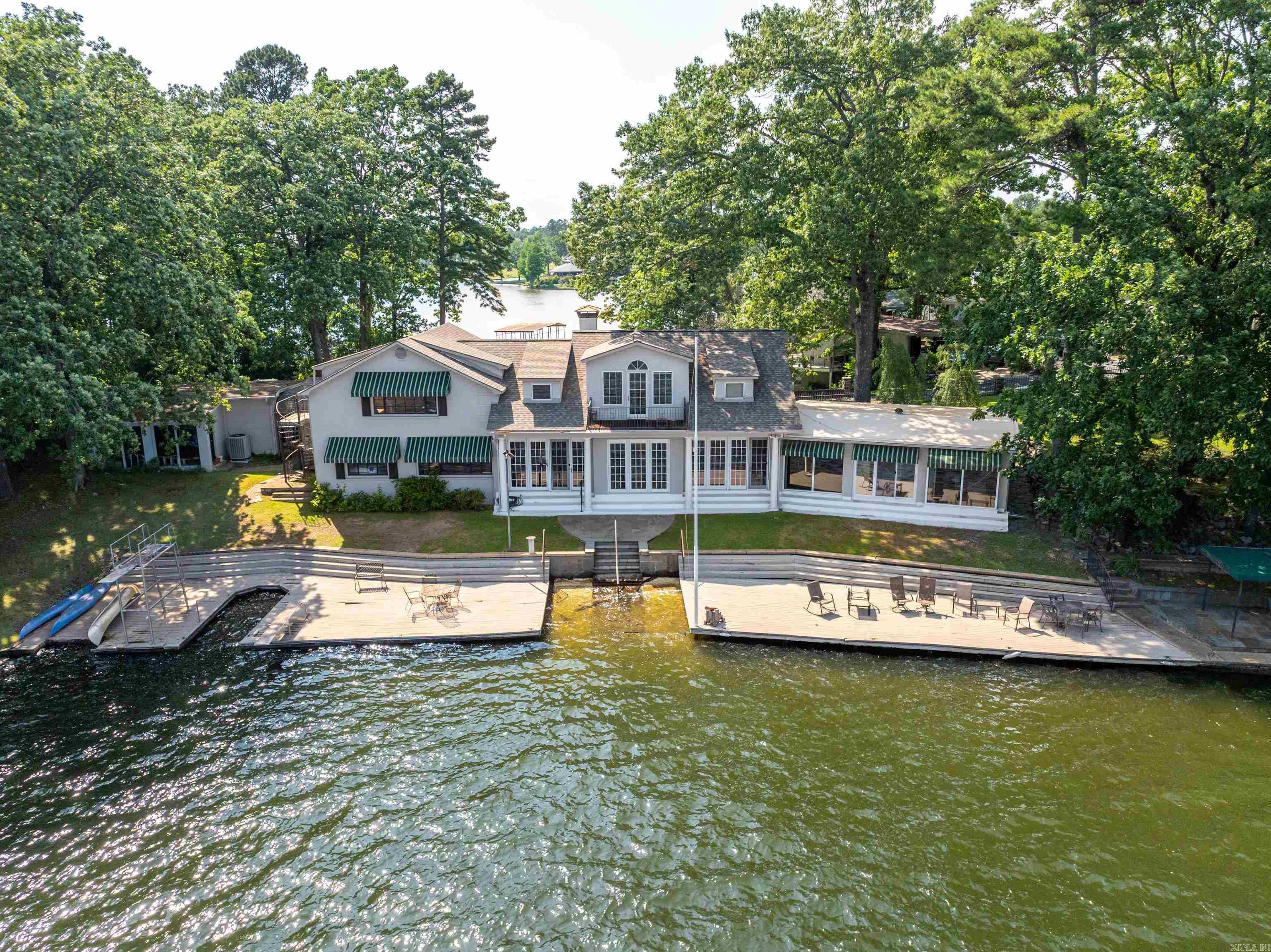 Come see this once-in-a-lifetime property perched on the shores of Lake Hamilton in Hot Springs, Arkansas! Situated near majestic  point, this extraordinary estate offers unparalleled breathtaking views of sunrises and sunsets on Lake Hamilton's serene waters. Whether sipping your morning coffee or hosting guests for dinner, you will be captivated by the natural beauty that is right outside your door. With plenty of area for outdoor living, you can enjoy direct access to the lake waterfront. Recreation and entertainment spaces are abundant with outside decks hovering right over Lake Hamilton. Dive into the serene waters from your own swim platform or moor your watercraft, or soak up the sun and take in the spectacular views that stretch for miles. The waterfront boathouse with two private slips is perfect for facilitating easy access to all sorts of water activities, including skiing, fishing, or leisurely cruises to soak up the sun. Spacious interiors abound in the 5-bedroom, 3-bath home, which spans 4992 square feet. Luxury details are evident throughout with vintage finishes and tasteful furnishings that enhance its ambiance.
