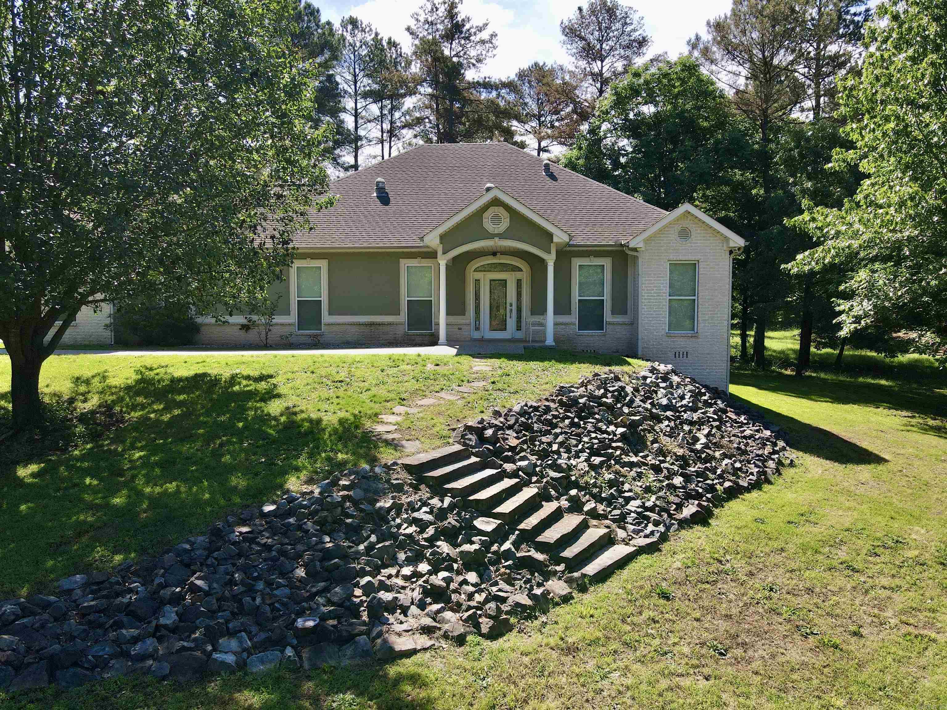 Located on nearly 3 acres in the desirable Brookhill area, 780 Brookhill Ranch Road offers privacy just minutes from the Hot Springs Village gates. This 2008 custom-built home features an open floor plan with vaulted ceilings and significant natural light from large windows and sun tubes. The interior is updated with new Green Guard Gold certified waterproof LVP flooring throughout. The kitchen includes custom cabinetry, ample workspace, and a large pantry, while the primary suite is designed with a functional office nook and a walk-in shower. Additional living space includes a heated and cooled sunroom for year-round use.  A standout feature of the property is the 60x40 detached shop with 6" thick concrete floor. This 3200 sq ft versatile building includes a partially finished, 20x40 loft equipped with full bathroom and washer hookup, making it ideal for a workshop or hobby space. The shop has an additional half bath on main level and has a heated/cooled area. This property efficiently combines a well-maintained residence with substantial utility and acreage.
