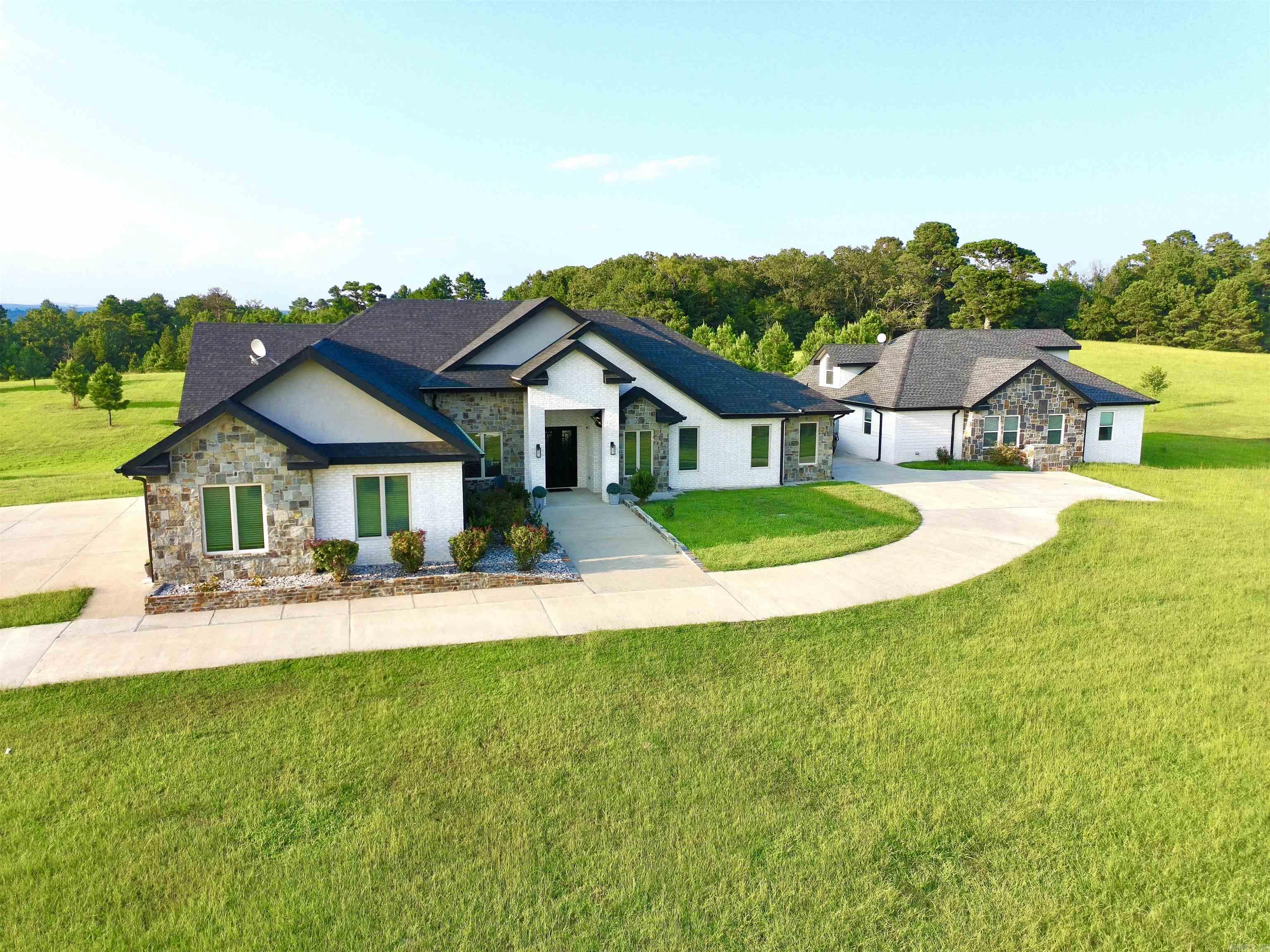 Dual-Home Private Estate on 6.8 Acres! Just 10 minutes from town, this rare property includes two full homes totaling 6 beds, 5.5 baths, and 5,311 sq ft.  The main 3,349 sq ft residence features an open floor plan, 3-car garage, office, and 3 ensuite bedrooms. The primary suite includes a soaking tub, oversized walk-in shower, and a large closet that doubles as a reinforced storm shelter. The chef’s kitchen has a double oven, high-end appliances, a large island with quartz waterfall countertops, and abundant counter space with custom cabinets. Expansive laundry room with extra storage, family room with 18-foot cathedral ceilings and rustic wood beams, and a private elegant office with 12-foot ceilings and built-in shelving.  The 1,962 sq ft guest home offers private parking and entrance, 3 beds, 2 baths, laundry, and a spacious loft with stunning Ouachita Mountain views—perfect for an office, library, or playroom.  Outdoor amenities include a shared 1,200 sq ft concrete patio, a 370 sq ft workshop/shed, a 10x10 chicken coop with 16 nesting boxes, and a fully fenced 10x20 chicken run.  This private retreat is ideal for luxury, multigenerational living!