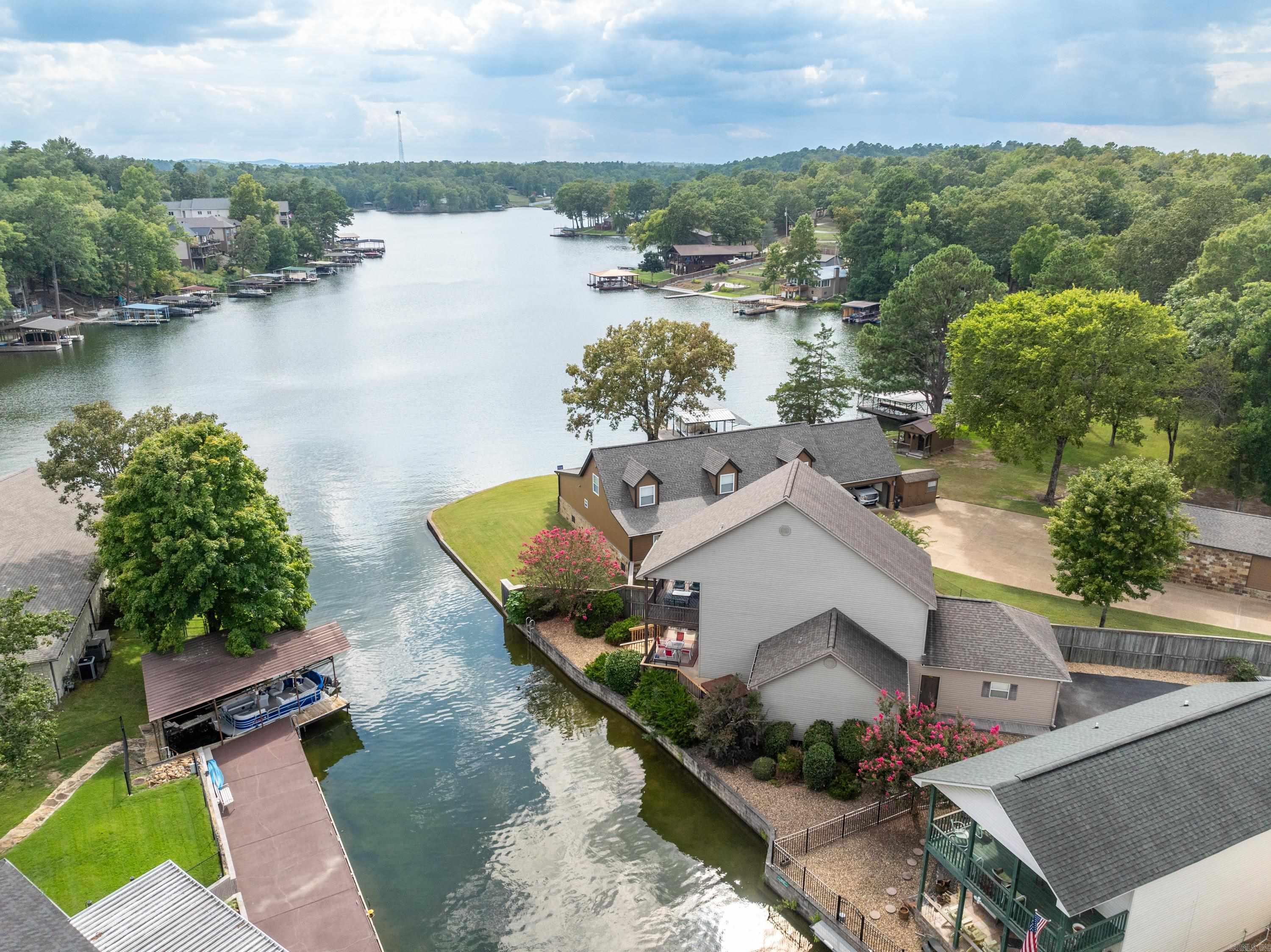 This 3-bedroom, 3-bathroom cottage is located in a quiet cove on the shores of Lake Hamilton. Situated just a few steps from the water, you can swim & fish from your back yard, soak in the hot tub while soaking up the views, or peacefully sway on the porch swing while enjoying the sunset. Upper and lower decks provide abundant space for entertaining/enjoying loved ones; and the boat tie-up along the seawall allows visitors by water & tenants to keep a boat during their stay. Inside, you'll love the open/airy concept with hardwood floors throughout the kitchen and living areas. You'll appreciate each bedroom having its own attached bath - with one suite on the main level and two additional suites upstairs. The two-car garage allows for convenient parking and extra storage. This property is a wonderful choice for a primary residence or investment property - with monthly/nightly rental history on file.  The property is currently rented through January 21st. Agents, see remarks.