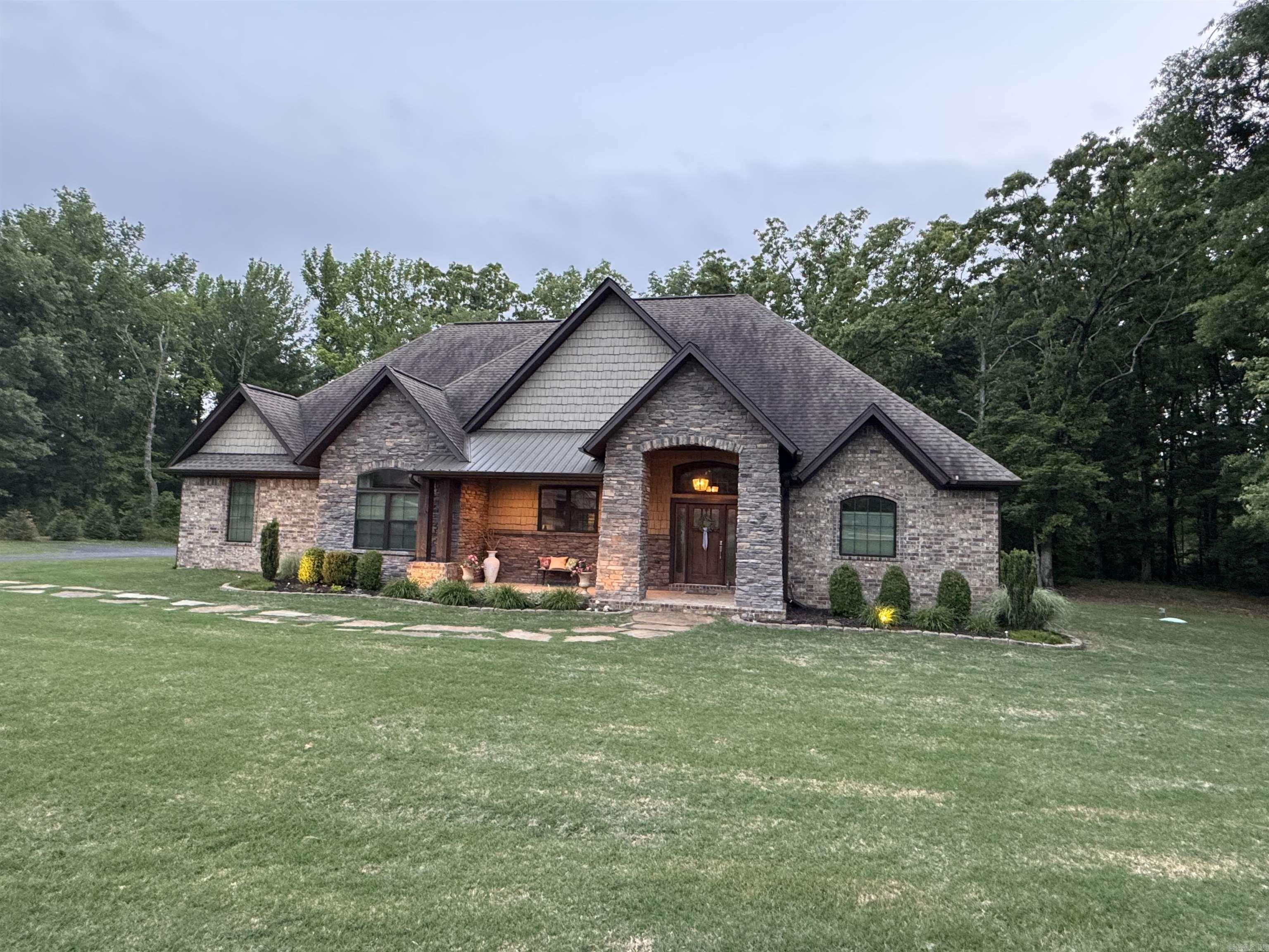 A custom home on 3+ acres just outside the Searcy city limits feels like country living but in a lovely well-maintained neighborhood. The home has a large bonus room/4th bedroom upstairs for visitors or movie night, but the rest of the living space is on the main floor. The living room has 18' vaulted ceiling with wood beams and has French doors to a vaulted covered patio. 100s of trees create a private backyard. Living and dining rooms are central and open to the front facing kitchen with granite countertops, a black wooden island, and stainless appliances including a gas range. The main floor features all concrete stained floors for low maintenance. The owners suite is large and includes 2 closet spaces, along with an en-suite bath with tile shower, free standing tub, and 2 vanities. All exterior walls are insulated concrete forms 10" thick for added efficiency and safety. Oversized 3 car garage with Electric car charger. Tankless gas water heater with instant hot water circulation. Enjoy neighborhood views from the front porch, or wooded views of nature from the back patio. Truly the best of both worlds. SEE AGENT REMARKS