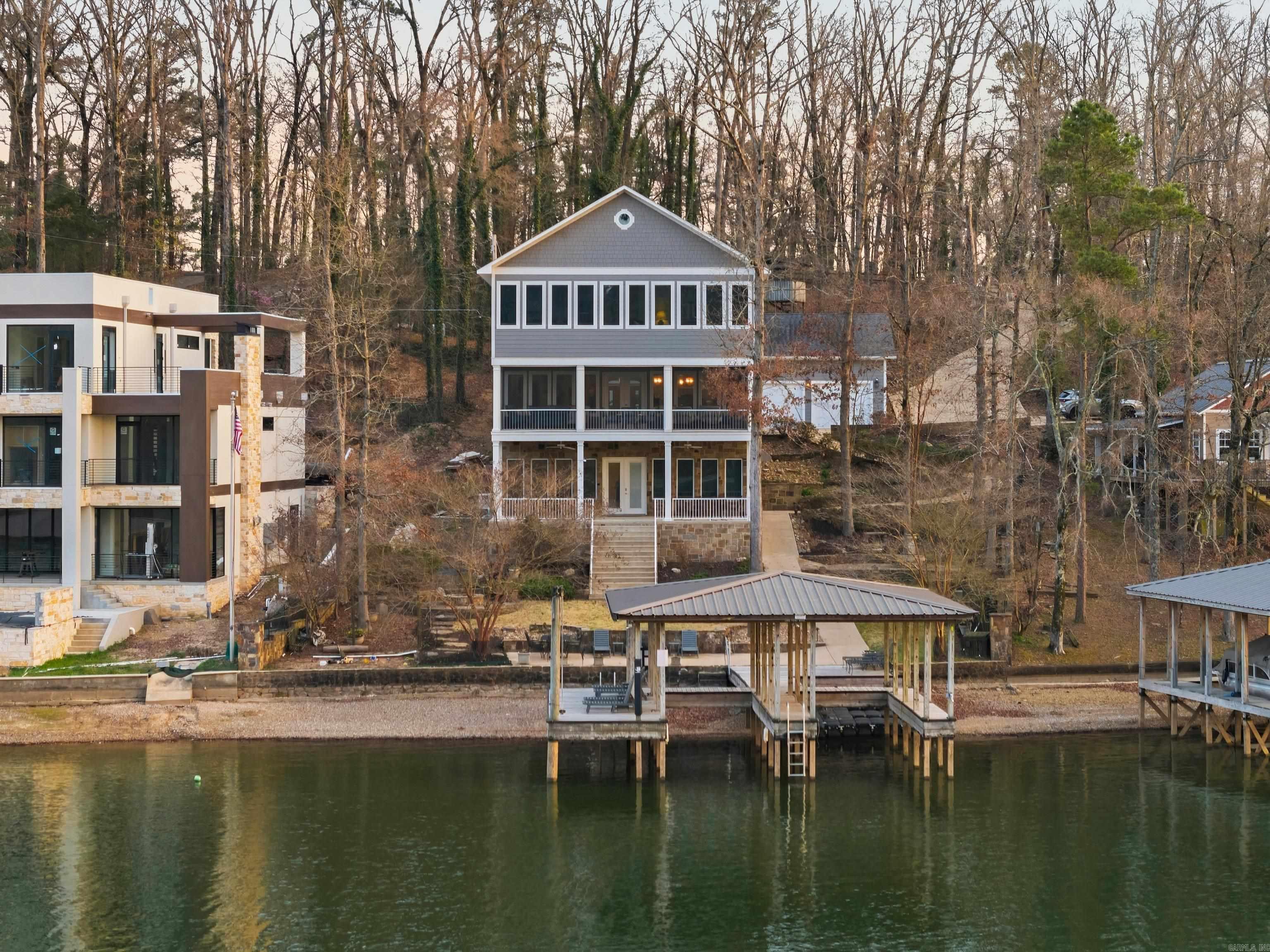Welcome to 350 Longpoint, a stunning coastal Southern lake house on Lake Hamilton. Built in 2016, this 5-bedroom, 3.5-bath home offers 4,896 sq ft of luxurious, relaxed living. Designed in a coastal Southern style, the home features a grand chef’s kitchen with an oversized granite island, double ovens, and double dishwashers, all flowing into a spacious dining area and open floor plan. Gather by the propane fireplace and enjoy serene views of a quiet cove across from Garvan Gardens. Upstairs, you'll find five spacious bedrooms, beautifully updated baths, and a game room or sunroom. Zoned HVAC with two units ensures comfort throughout. Downstairs entertainment level with pool table, second kitchen, dining area, and a huge living space perfect for family fun. The home includes a rare 5-car garage, stone accents, and a firepit, with multiple decks perfect for entertaining lakeside. A double-stall, stationary covered boat dock completes this exceptional oasis.