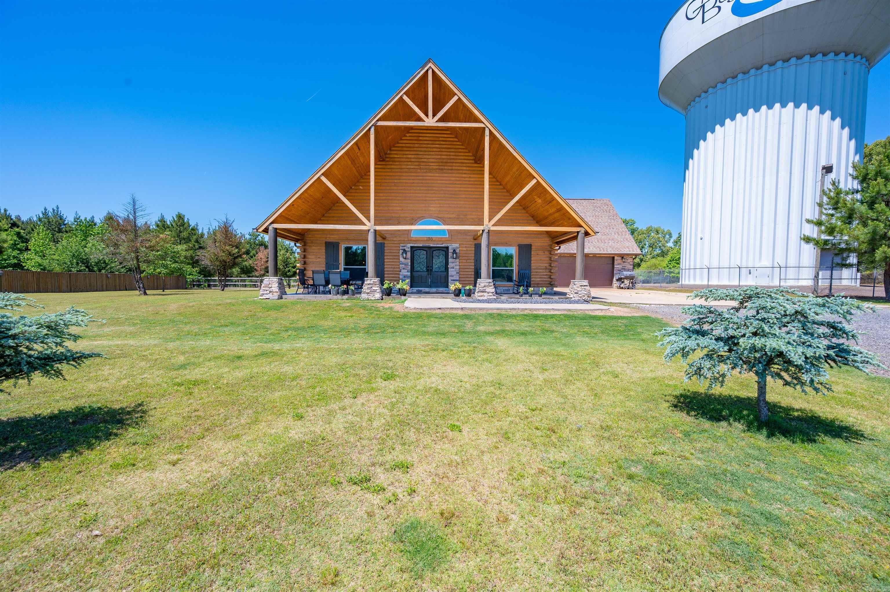 Don’t let the water tower deter you! What better neighbor to have, than one that never complains and makes zero noise! Situated on 5.96 acres that is beautifully maintained, this stunning log home offers privacy and room to roam! Need a place for horses, chickens and all the animals for farm life? The property is fenced with an electric fence, electric gate and an outbuilding/barn for the animals and a separate small shop area w/single garage door. Start your day with a cup of coffee on the massive front porch. When it is time to go in, step inside the double doors to a breathtaking, open concept living area w/fireplace and a soaring vaulted ceiling. The kitchen is a chef’s dream with a 6 burner Thor gas stove w/double ovens and griddle area. When you are ready to retire for the evening, there are 4 bedrooms and 3 baths. Worried about the weather? That is covered as well! The home features a large safe room and a 22k Generac generator! This home has so much to offer! Book your showing today! AGENTS PLEASE SEE REMARKS.