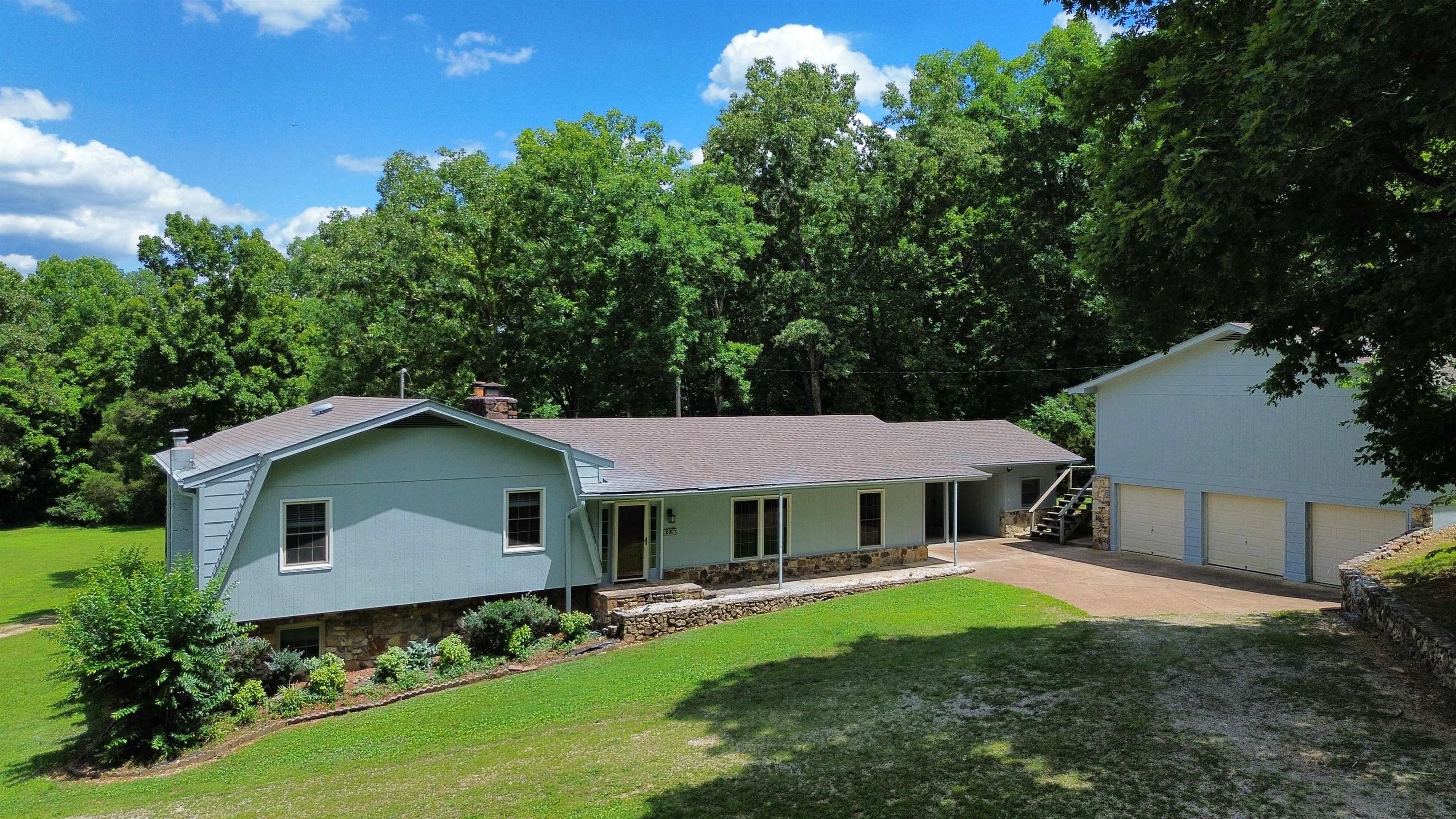 Tucked away on 13.62± surveyed acres in the rolling Ozark hills, this Rainbow Lake retreat offers the rare combination of privacy, space, and convenience. Surrounded by mature trees and abundant wildlife, you’ll feel miles from it all while downtown Hardy and the world-famous Spring River are less than five minutes away. Inside, a striking floor-to-ceiling native stone fireplace, vaulted ceilings, warm wood floors, & a spacious custom kitchen with ceramic tile create an inviting place to gather. The screened porch overlooks peaceful woods and provides the perfect spot for morning coffee or quiet evenings. The top level features a spacious primary suite with a large walk-in closet, plus a laundry chute while the lower level offers an additional 2 rooms, full bath, laundry area, & extra storage. Outside, the detached 3-car garage includes a huge unfinished upper level ready for guest quarters, an apartment, game room, studio, or workshop. With a brand new heat pump, fresh coat of paint, 2022 architectural roof, city water and sewer, cleared lawn areas, outside storage buildings, & possible chicken coop!