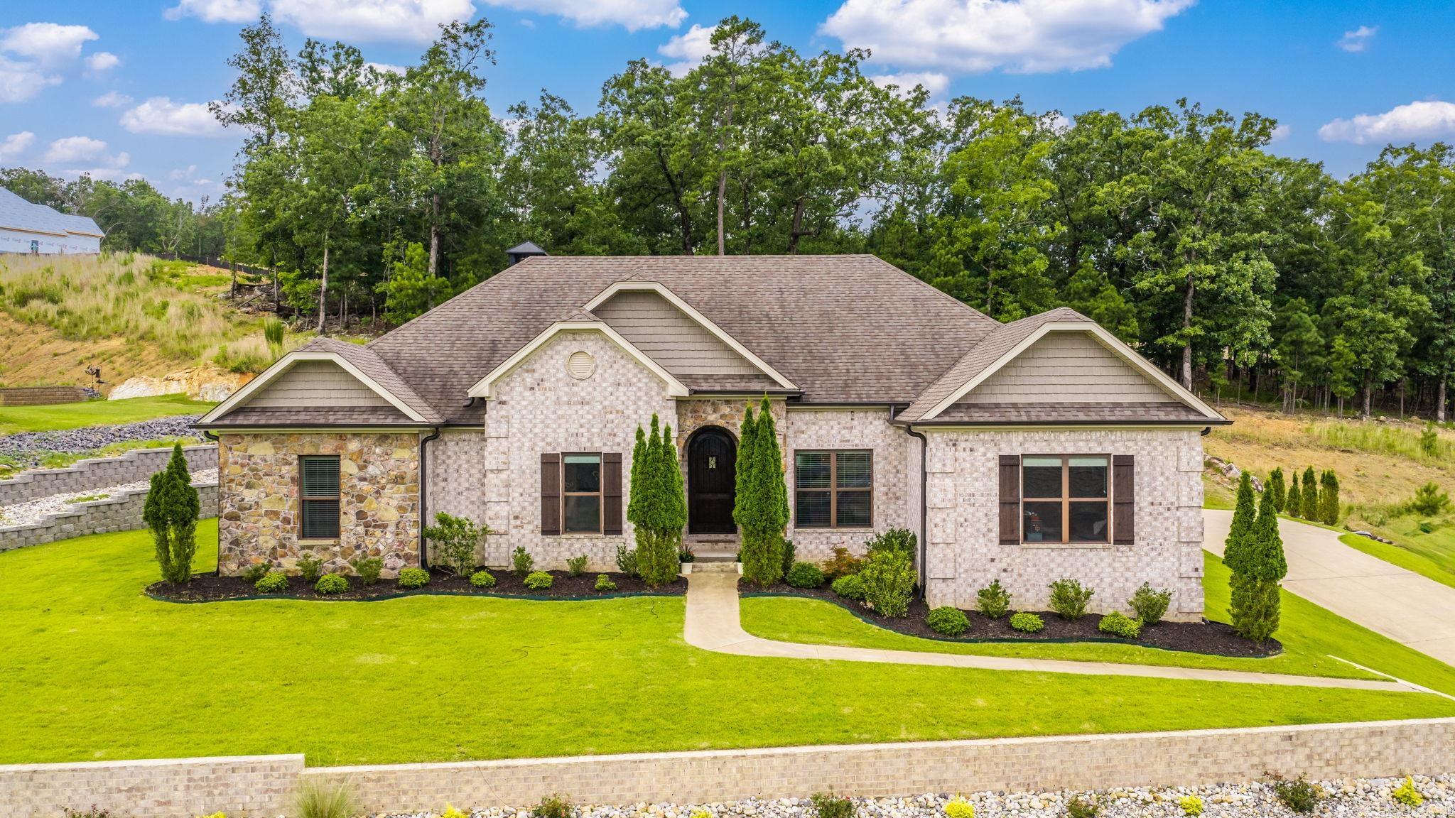 Perched atop the ridge in the new Eagle Ridge community of Maumelle Valley Estates, this stunning custom home delivers one of the area's most breathtaking  views and the lifestyle to match. Set on OVER half an acre, this four-bedroom, three-bath masterpiece features a versatile bonus room and was built to impress from the ground up. Expert added landscaping and an artfully designed dry creek bed with French drains elegantly and efficently redirect mountaintop runoff, keeping this hilltop retreat as pristine as it looks. Step inside to discover soaring ceilings with contemporary lighting, rich hardwood floors, and a cool coastal open floor plan that flows effortlessly — all anchored by gorgeous quartzite stone finishes that truly set this home apart. When the day winds down, step outside to your covered patio where a built-in fireplace frames peaceful views of the lush green space beyond. Priced to sell, a home this unique and this special rarely comes along — don't miss your chance to make it yours.