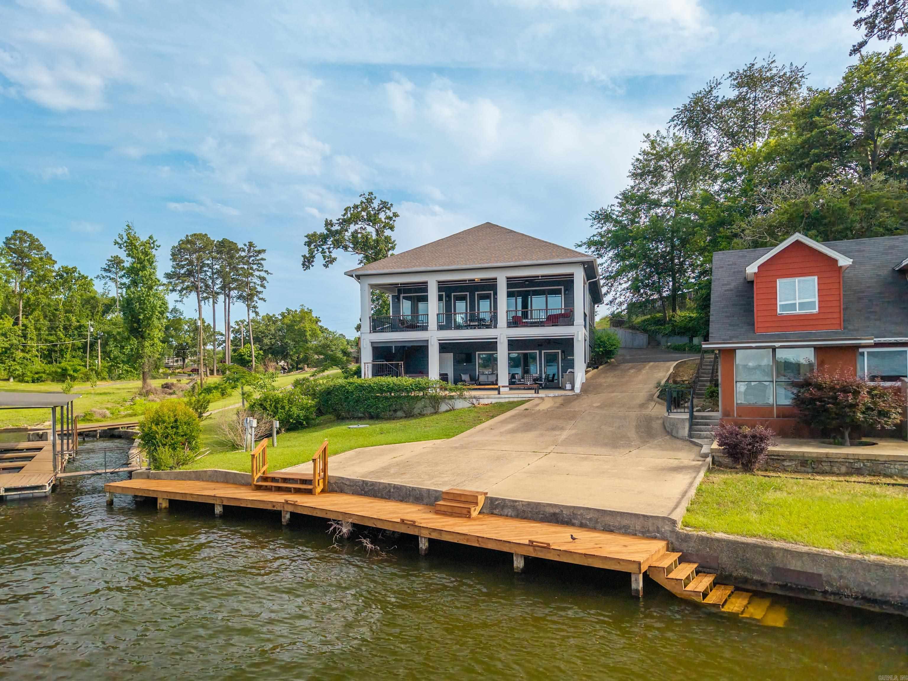 Luxury Lake Hamilton Waterfront Retreat! Approximately 3,200 sq. ft. of beautifully updated living space with breathtaking lake views and a proven short-term rental history. The open-concept upper level features a spacious living area, dining space, gourmet kitchen, and a private primary suite with deck access and stunning waterfront views. The lower level offers a second living area, secondary kitchen, two additional bedrooms, full bath, half bath, and second laundry area—ideal for guests or multi-generational living. Recent updates include brand-new luxury flooring, fresh paint, and a new roof in 2024. Enjoy outdoor living with an outdoor kitchen, hot tub spa, and lakefront boardwalk. Sold fully furnished for a true turnkey opportunity. Permit already approved for a specialized boat dock. Whether you're looking for a luxury waterfront home, vacation retreat, or investment property, this Lake Hamilton gem is ready to enjoy! See Agent Remarks
