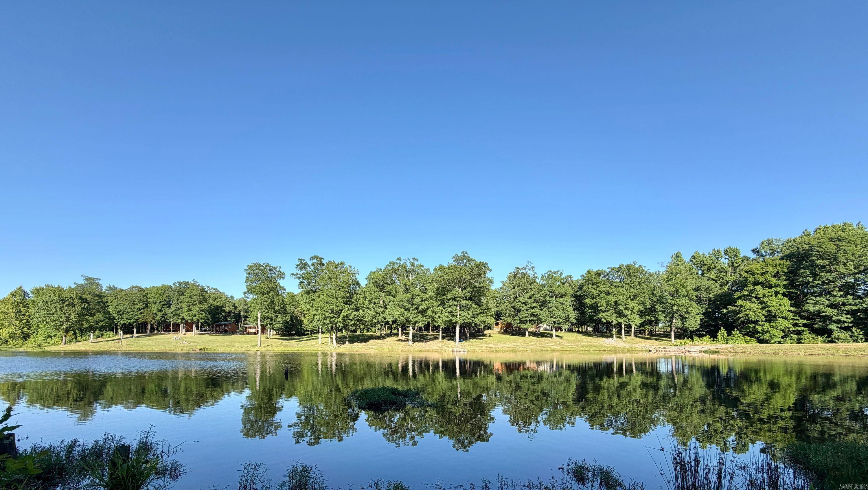 From the moment the gates open, this incredible 31 +/- acre Ozark retreat in Floral, Arkansas featuring 4 cabins, a large 8-acre lake, shop, trails, greenhouse, garden, and resort-style amenities immediately captures your attention. Located just 15 minutes from Batesville, this one-of-a-kind property is ideal for a family compound, private retreat, Airbnb investment, or event venue. Property features a stunning true cedar log cabin with 3 bedrooms, 2 bathrooms, vaulted ceilings, exposed cedar throughout, skylights with motorized solar blinds, a floor-to-ceiling rock fireplace, covered front and back porches, and beautiful tile flooring with the look of wood. Three fully furnished guest cabins overlook the stocked lake, each offering covered front porches and outdoor grilling areas—just bring your clothes. Additional improvements include a fully equipped shop with attached carport, large kennel area, custom brick smoker, pumphouse, RV hookup, and an outdoor wood boiler system heating both the main cabin and shop. Irrigated greenhouse, deer fencing, solar-powered electric fencing, and water supplied by a ram pump and solar pump. Trails, fruit and nut trees, and solar-lit driveway.