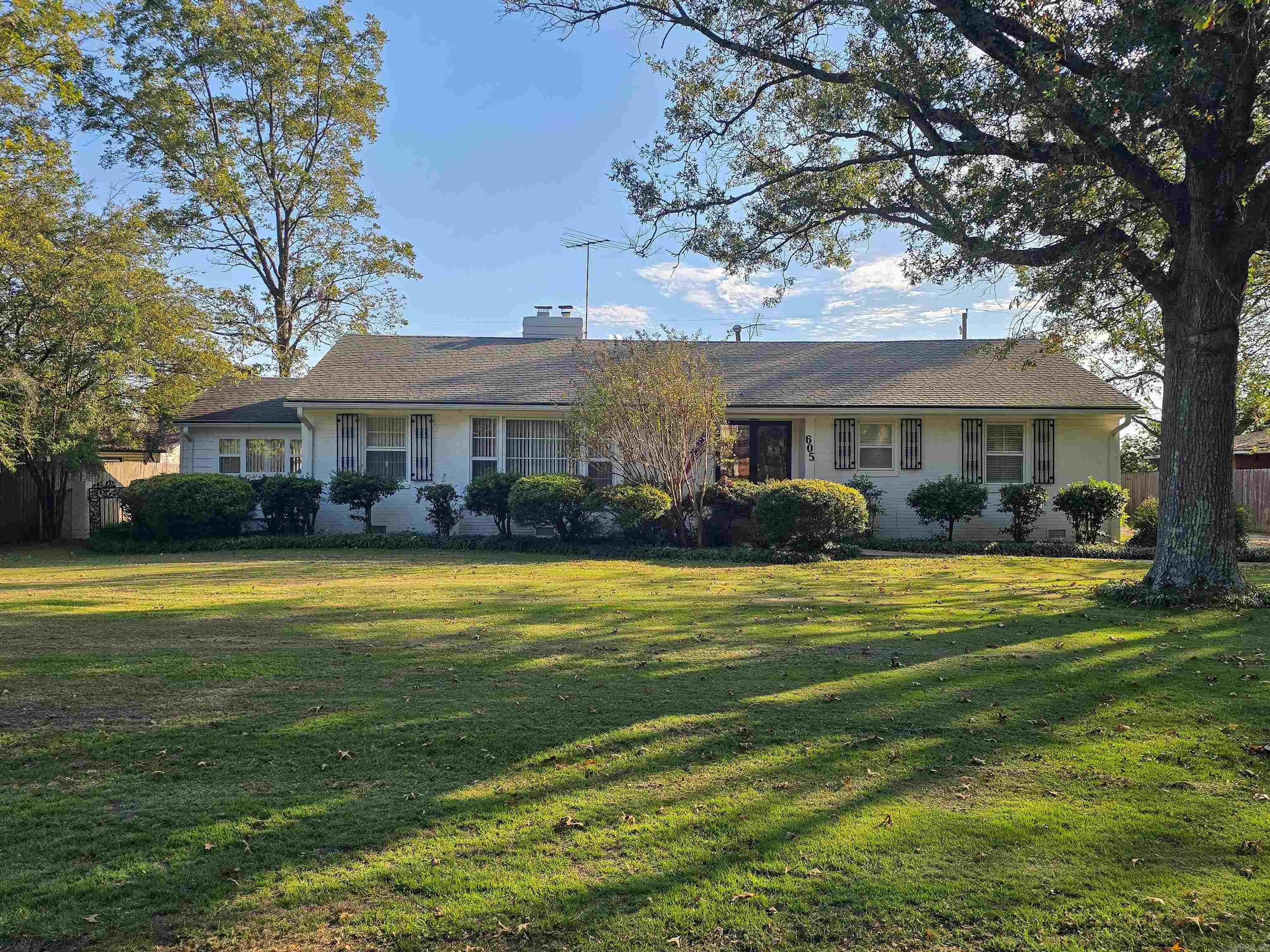 Spacious and full of charm, this 3-bedroom, 3-bath home offers an impressive layout with multiple living areas and excellent storage. The formal living room welcomes guests with large picture windows, crown molding, and its own cozy fireplace. The formal dining room features a stunning waterfall mural for a one-of-a-kind backdrop when entertaining. The kitchen offers extensive cabinets, counter space, built-in breakfast bar, large pantry, and a 3-compartment sink plus a bar sink. A convenient laundry closet is nearby. The oversized primary bedroom includes a walk-in closet and private bath, while the additional bedrooms each have great closet space and character. The massive den showcases rich wood built-ins and a large brick woodburning fireplace. Step outside to an extra-large patio overlooking the tree-shaded yard with beautiful tulip trees. Dual 11x8.5 storage rooms under the carport offer space for tools or hobbies. A Generac generator provides peace of mind. A truly extraordinary home with timeless appeal.