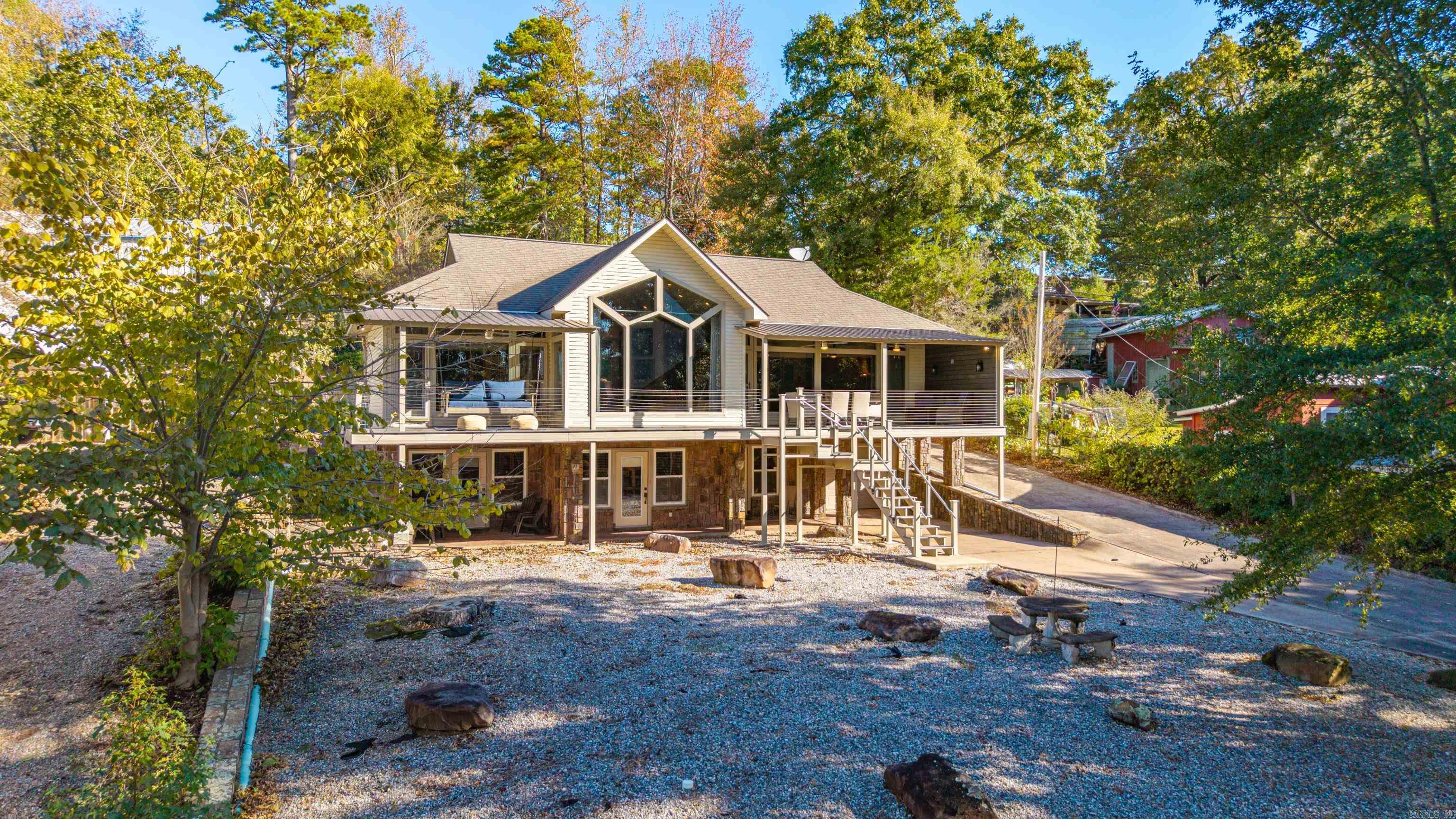 Sweeping Lake Greeson views from this custom-built retreat on a quiet Kirby street! This 2,468 SF home sits on .38 acres with stunning vistas across Corps-protected land. Entertain on the expansive composite deck with an electric fireplace, or relax on the additional covered patio. Inside, soaring vaulted ceilings with an electric fireplace and floor-to-ceiling windows frame water views from every room. Gourmet kitchen features double Dacor ovens, premium appliances, pantry, wet bar & laundry room. Primary suite on main level; 3 additional bedrooms below. Dual HVAC zones, tankless water heater, 2x6 exterior walls. 1-car garage plus covered parking for 2 vehicles. The garage provides excellent storage for water toys and lake gear. Hidden safe room off bookcase. Beautifully landscaped with 20' waterfall water feature. Minutes to Self Creek Marina for boat slips & rentals. Easy access to boating, fishing, hiking, and ATV trails. No HOA. Turn-key lakeside living at its finest!