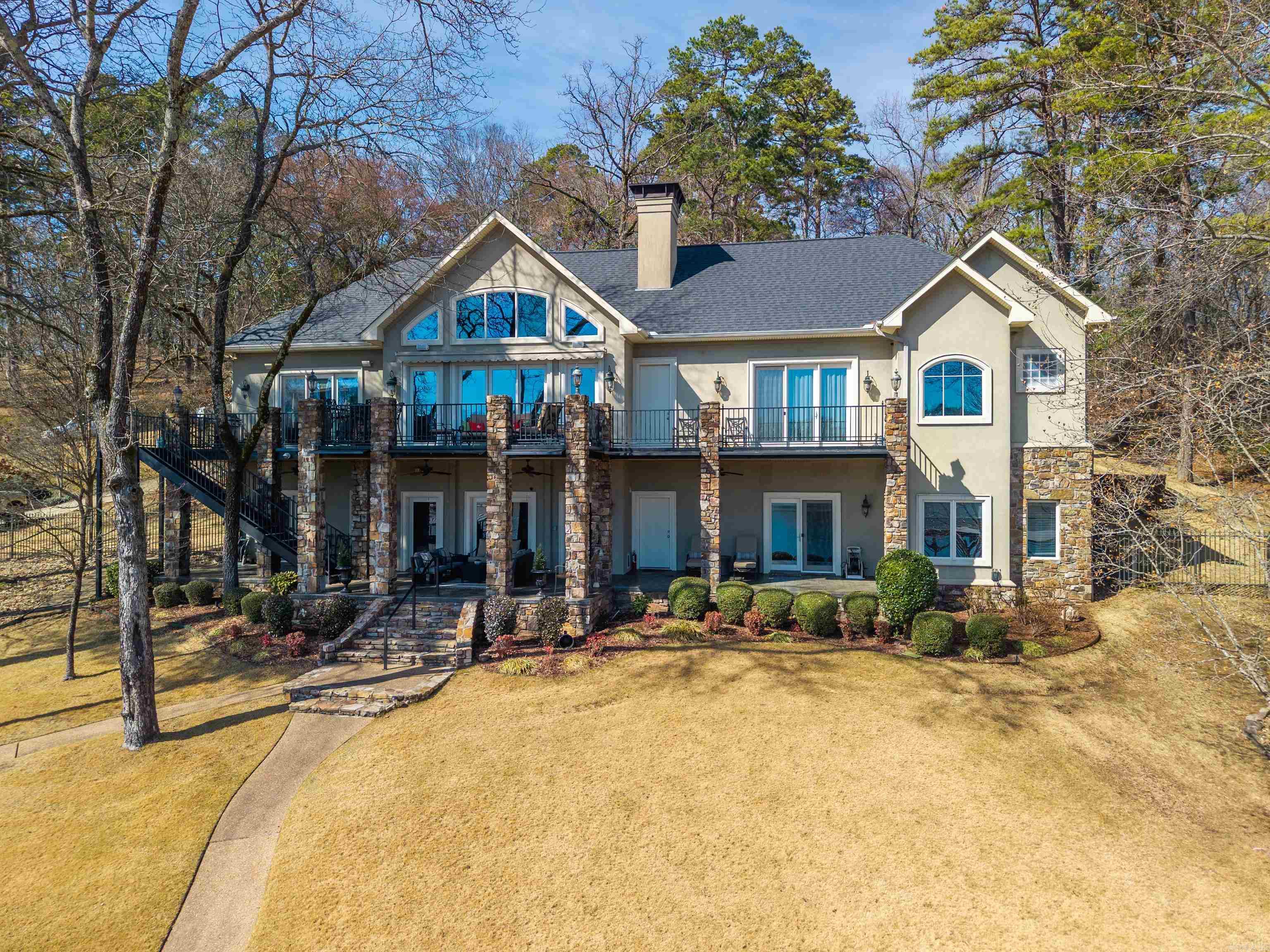 Experience luxury lakefront living at its finest on the pristine shores of Lake Hamilton. This stunning custom-built estate offers an impressive 179 feet of private shoreline and over 5,100 square feet of thoughtfully designed living space, perfectly blending elegance, comfort, and breathtaking waterfront views. With six spacious bedrooms and six and a half baths, this home was designed for both grand entertaining and private relaxation. Each bedroom features its own en-suite bath, providing exceptional comfort and privacy for family and guests alike. Expansive windows throughout the home frame panoramic lake views and fill the interior with natural light. The primary suite is a true retreat, offering serene water views, generous proportions, and a luxurious en-suite bath designed for relaxation. A separate office space provides the ideal setting for remote work or quiet study while still enjoying the peaceful lake atmosphere. Step outside and discover an entertainer’s paradise. Multiple outdoor living areas create seamless indoor-outdoor flow, perfect for hosting gatherings or enjoying tranquil evenings by the water.