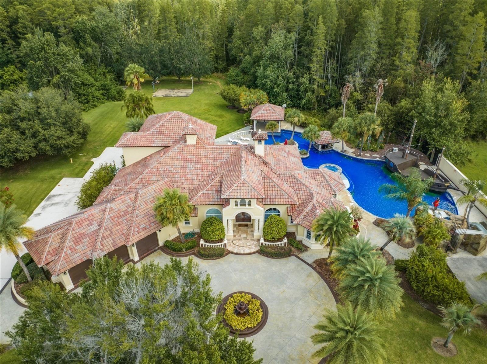 There are homes… and then there are experiences you never want to leave.

Tucked behind private gates on over 7.5 acres in one of Lutz’s most sought-after locations, this estate isn’t just a residence—it’s your own secluded world. A place where mornings begin in total privacy, and evenings feel like you’ve checked into a five-star resort… without ever leaving home.

As you arrive, the noise of everything else disappears.

You step inside and are immediately met with volume, light, and intention—soaring ceilings, sun-drenched living spaces, and an effortless open layout designed for both grand entertaining and quiet moments. The living room wraps you in floor-to-ceiling windows, while a fully equipped wet bar—with ambient LED lighting and electric shades—sets the tone for unforgettable nights with friends and family.

The kitchen isn’t just a place to cook—it’s where everything happens. Outfitted with commercial-grade appliances and positioned to overlook the entire backyard oasis, it becomes the heartbeat of the home—whether you’re hosting an event or enjoying a slow Sunday morning.

And then… there’s your escape.

The primary suite is its own private retreat—expansive, quiet, and intentional. Dual oversized walk-in closets, a private office with calming views, and a spa-like bath with a soaking jacuzzi tub and walk-in shower create a space that feels more like a luxury hotel than a bedroom.

Every guest experiences that same level of comfort, with four additional ensuite bedrooms, a second office, and a dedicated pool bath—because in a home like this, everyone lives well.

But the real magic?

It happens the moment you step outside.

This is where the story changes.

The backyard isn’t a backyard—it’s a destination. A $1.5M, 120,000-gallon resort-style pool unfolds in front of you like something out of a private island retreat. A hidden cave. A sunken bar. Waterfalls cascading into a lagoon. An outdoor kitchen ready for nights that turn into mornings.

And then—because ordinary was never the goal—a 45-foot concrete pirate ship rises from the water, complete with water-firing cannons and a fully air-conditioned interior lounge. It’s bold. It’s unforgettable. It’s the kind of feature that turns a home into a legend.

This is where parties happen. Where memories are made. And YOU never want to leave.

Beyond the experience, the estate delivers true functionality—3-car garage, over 200 feet of finished RV driveway with full hookups, reverse osmosis water system, updated interiors, and complete freedom with no HOA and no flood insurance required.

And while it feels like a private escape, you’re still just minutes from everything—Downtown Tampa, the airport, Armature Works, world-class dining, and premier shopping—all within a 20-minute drive.

This isn’t just where you live.

This is where life happens bigger.

This is where you host, escape, celebrate, and reset.

This is your private resort.