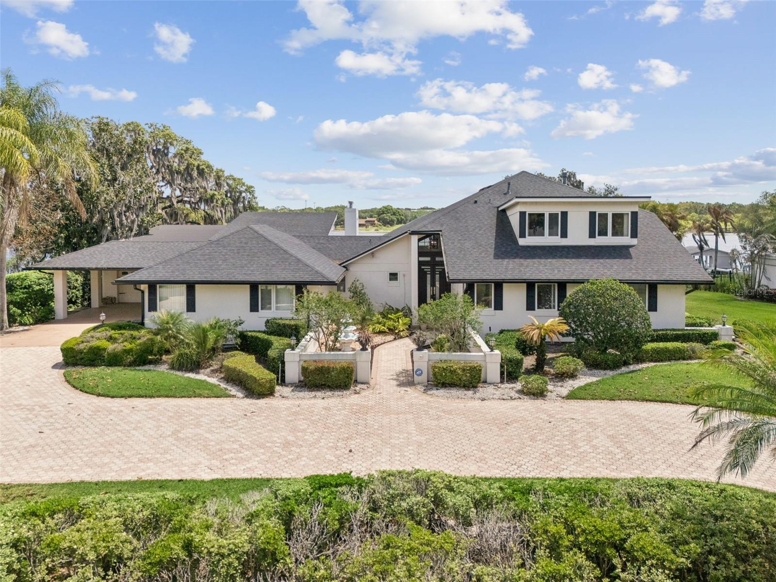 Lakefront estate on Lake Down in the Butler Chain of Lakes with over 150 feet of frontage and no HOA in Sunset Bay. Built in 1983, this 5 bedroom, 4 bath pool home offers nearly 7,000 square feet across three levels and presents a rare opportunity to renovate a true chain-of-lakes property to your own style and standards. Home retains much of its original character and is priced accordingly, creating strong value for buyers seeking premier waterfront frontage, square footage, and long-term upside in one of Windermere’s most desirable locations. Main level includes kitchen, dining area, secondary bedrooms, full baths, oversized laundry room, and sliding doors opening to covered outdoor living and lake views. A few steps down, the sunken living room features a bar, fireplace, storage, and direct water views. Upstairs, the primary suite includes a fireplace, large walk-in closet, dual vanities, tub, separate shower, and screened balcony overlooking the lake. This level also includes a private office. The lower level is a standout feature, offering a full basement living space with its own kitchen, living room, bedroom, full bath, and direct pool access, ideal for extended family, guests, or multigenerational living. An additional reinforced interior room provides flexible use as a secure safe room, storm shelter, private storage room, or secluded flex space. Outdoor features include a screened pool, covered entertaining area, fenced yard, and private dock with space for two boats and two jet skis. Garage space accommodates up to 6 cars, plus a 2-car carport and a large circular driveway that provides additional parking for guests, larger households, or recreational vehicles. Additional storage areas and the lower-level garage create excellent space for boat gear, kayaks, paddle boards, trailers, and lakefront equipment. Home is priced in line with its recent appraisal, with the value reflecting both its current condition and the renovation investment a future owner may choose to make. For buyers seeking a large lakefront footprint, multigenerational layout, extensive parking, and the ability to modernize to today’s standards, this property offers a rare value on the Butler Chain. Located minutes from downtown Windermere, Restaurant Row, golf, shopping, and major attractions.